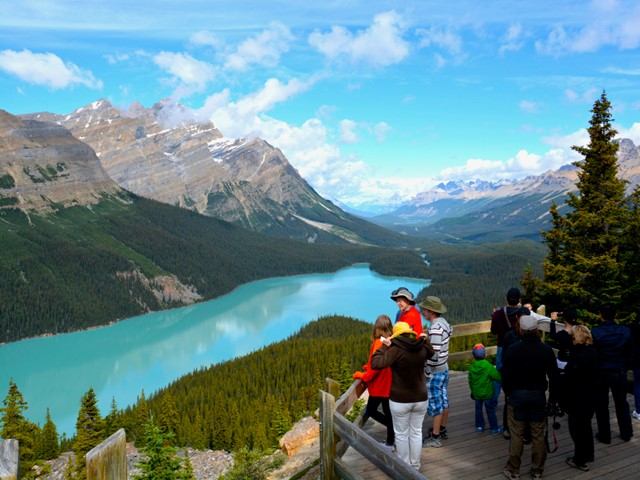 People standing at a lookout overlooking a bright turquoise lake and mountain valley.