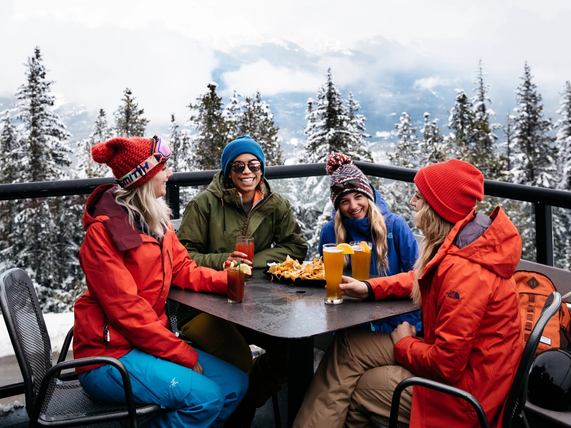 Friends enjoying drinks outdoors in snowy mountains at Marmot Lodge.