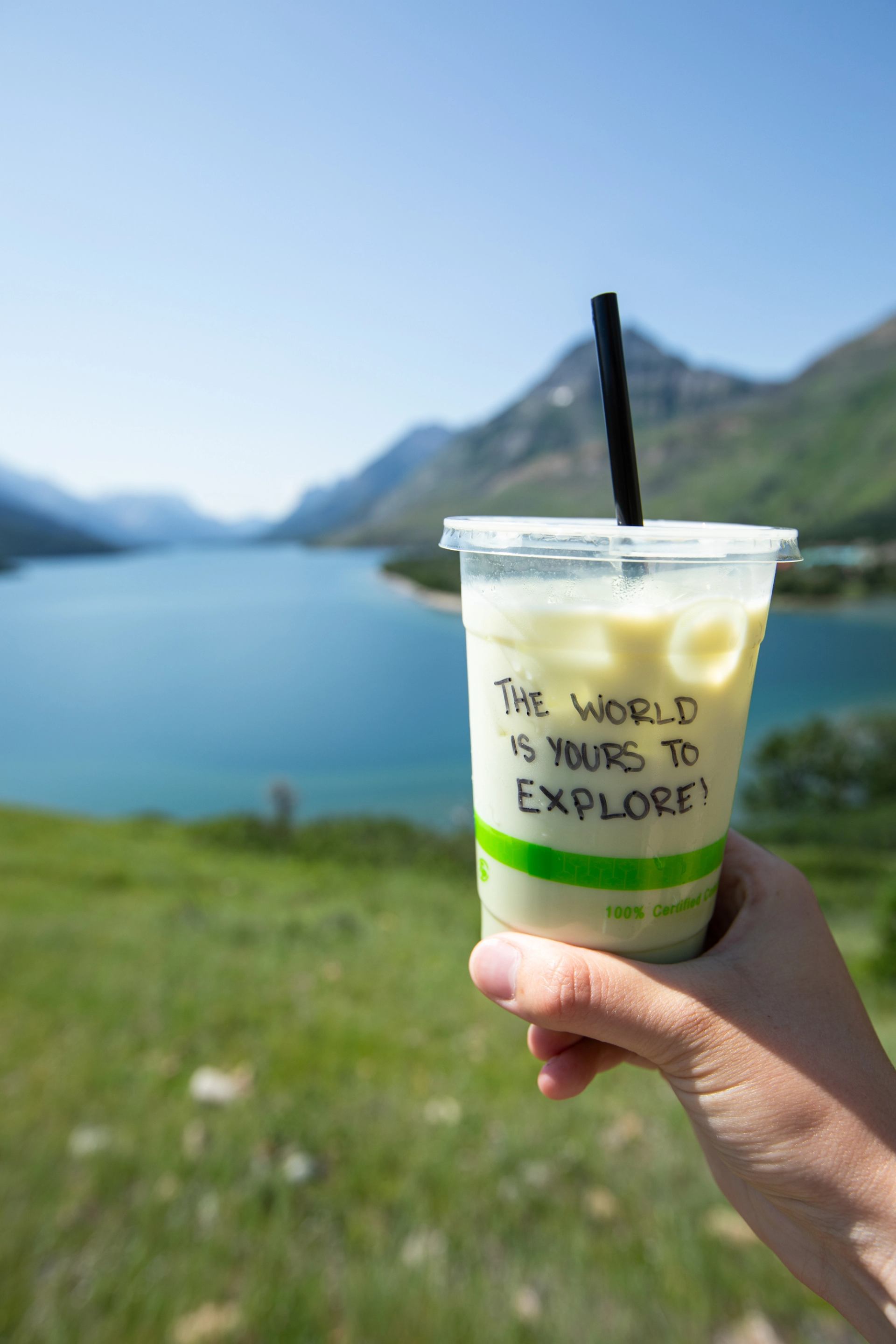 Iced coffee from Switchback Micro‑Cafe held up with a blue lake and mountain backdrop.