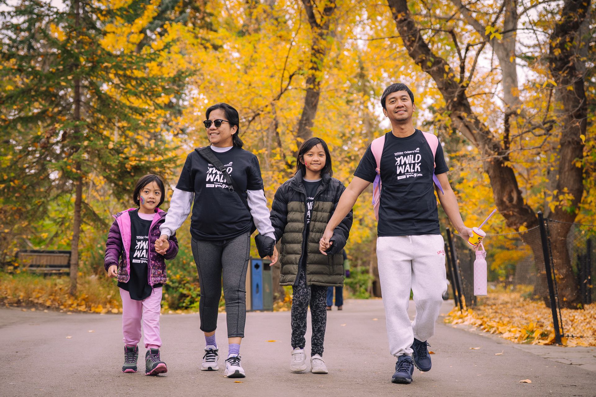Group wearing Wild Walk shirts walks hand in hand beneath yellow autumn foliage.
