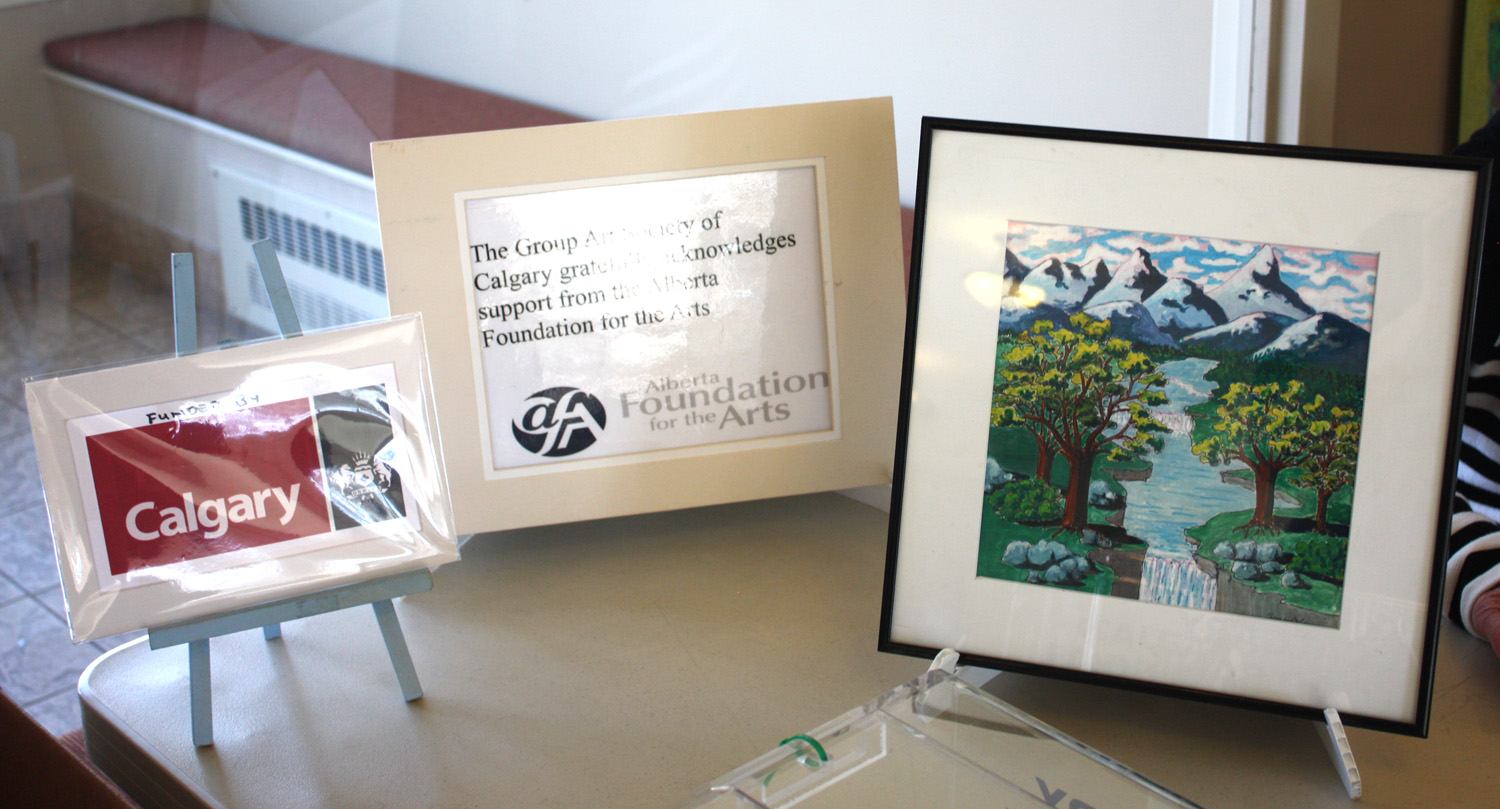 Framed mountain landscape painting beside Calgary and Alberta Foundation for the Arts display cards.