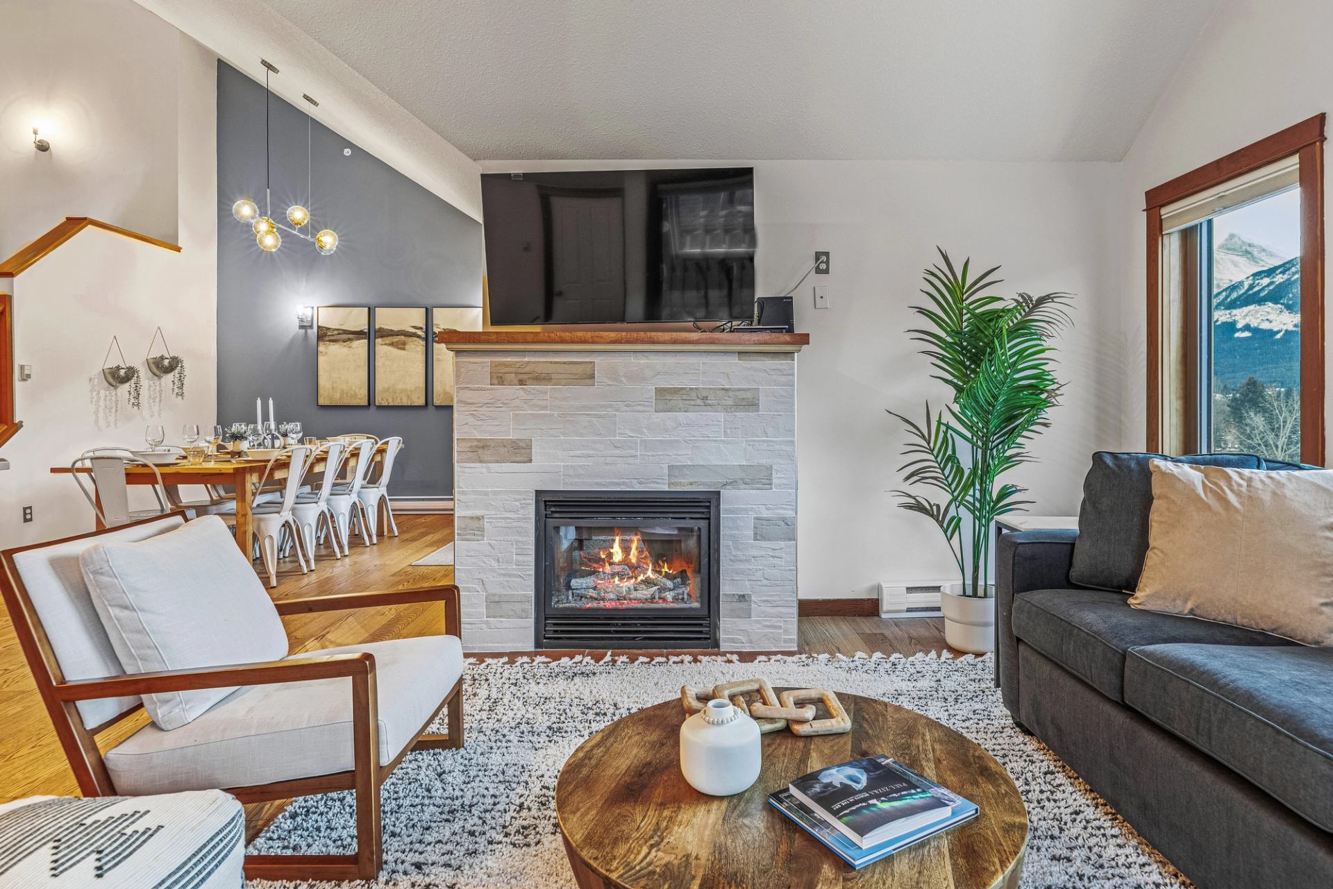Modern living room with fireplace, TV, dining table and mountain view through window.