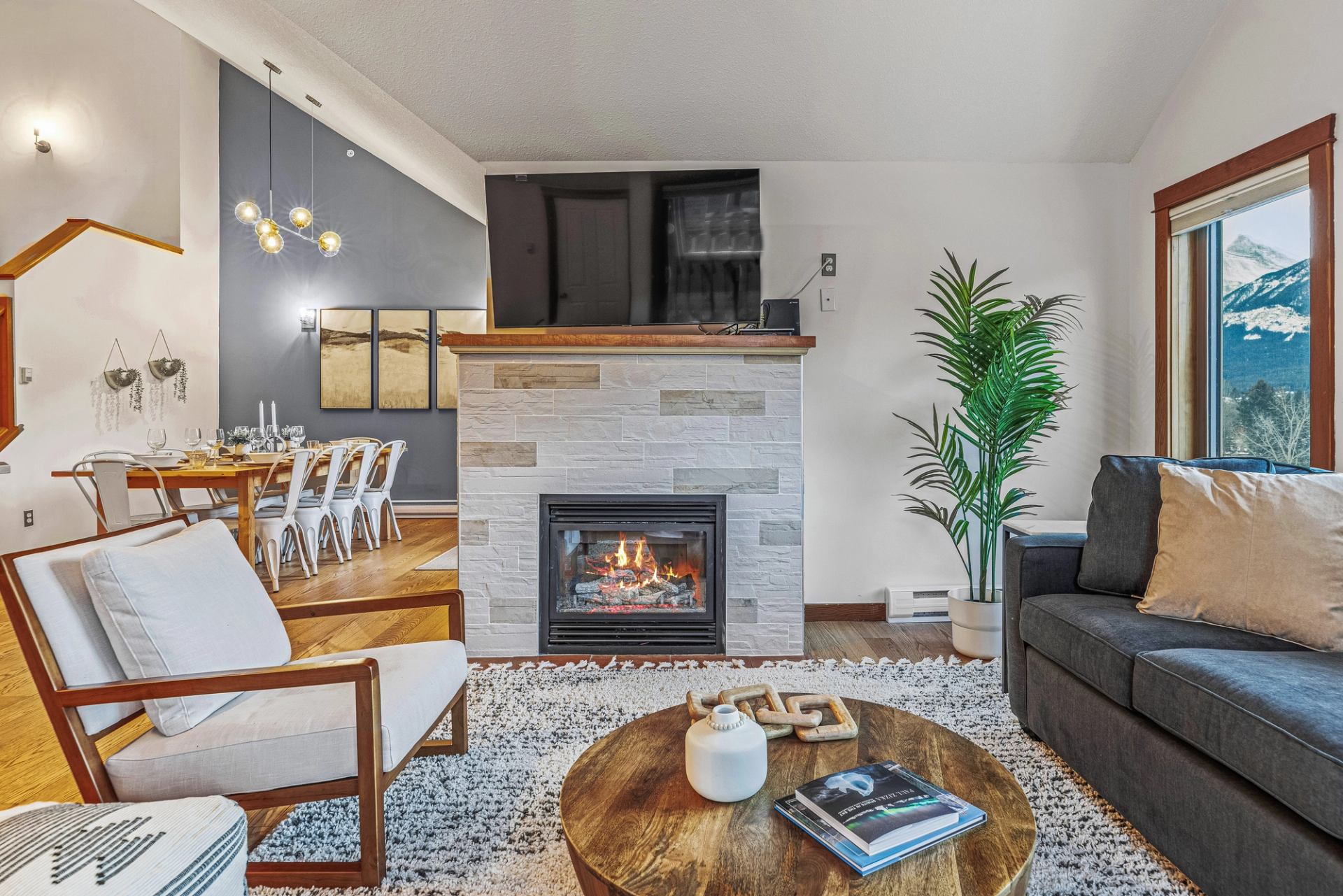 Modern living room with fireplace, TV, dining table and mountain view through window.
