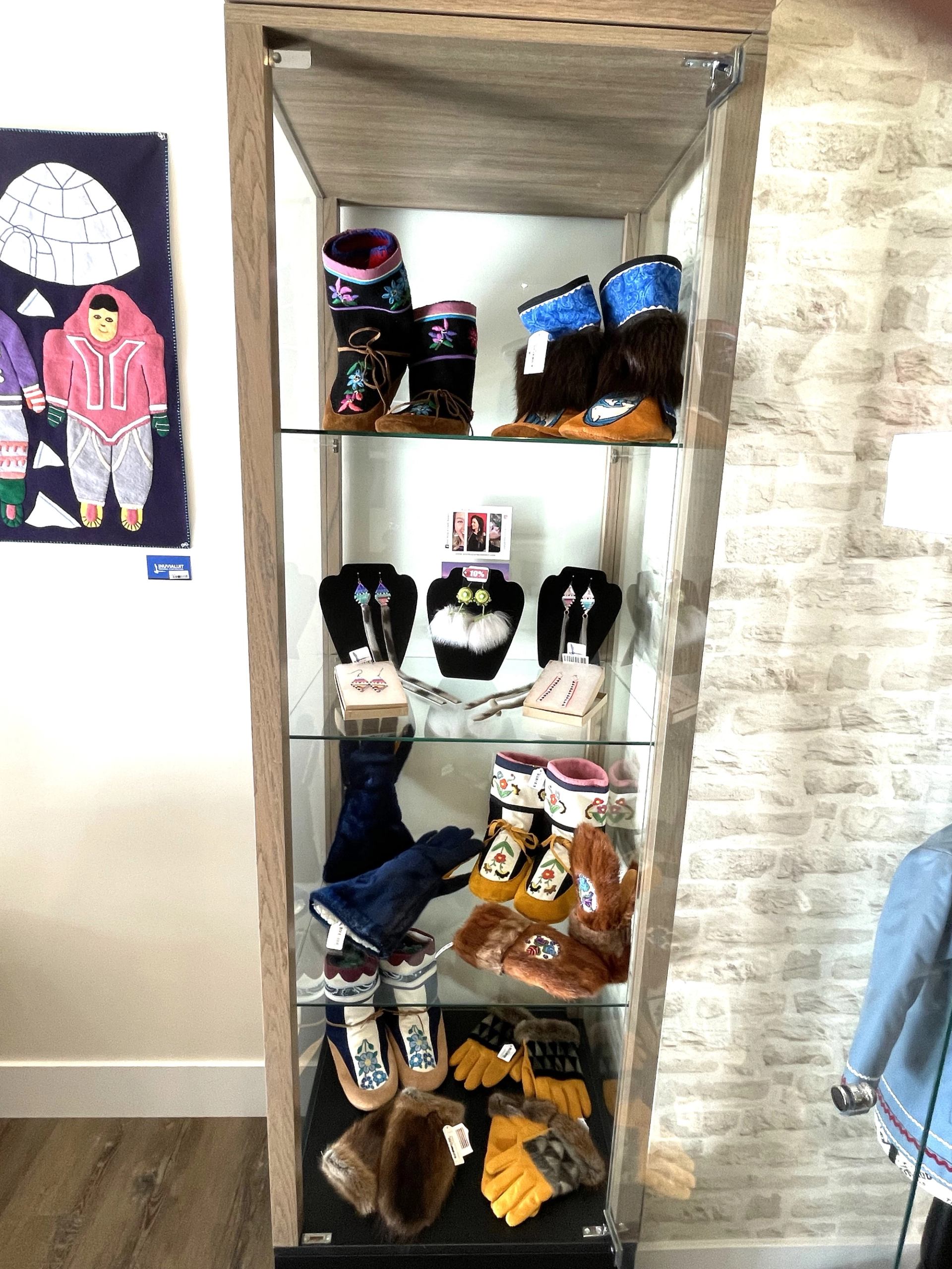 Glass display cabinet with embroidered boots, mittens, and jewellery in a retail shop.