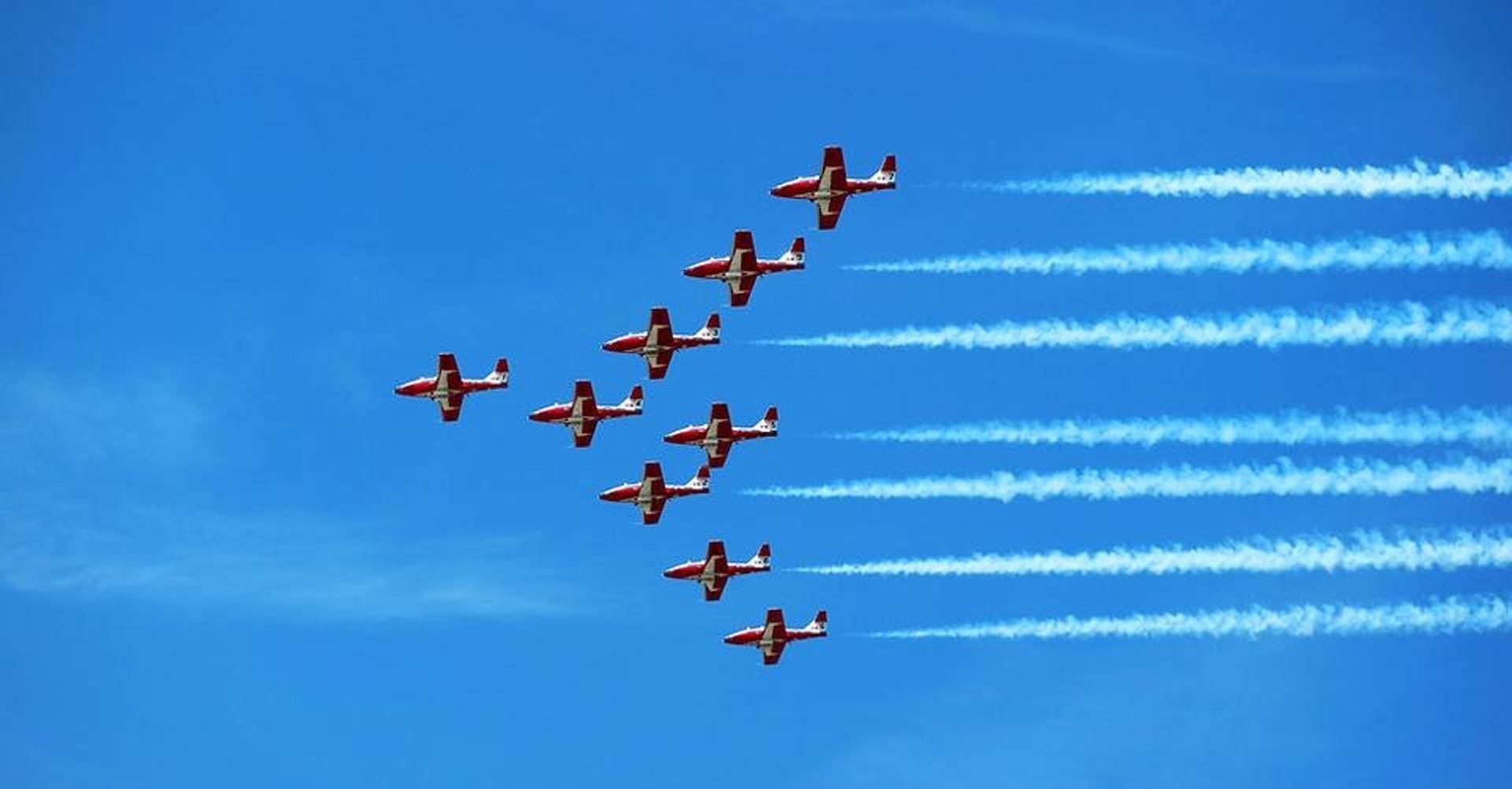 Red and white aerobatic jets fly in formation, leaving parallel white smoke trails.