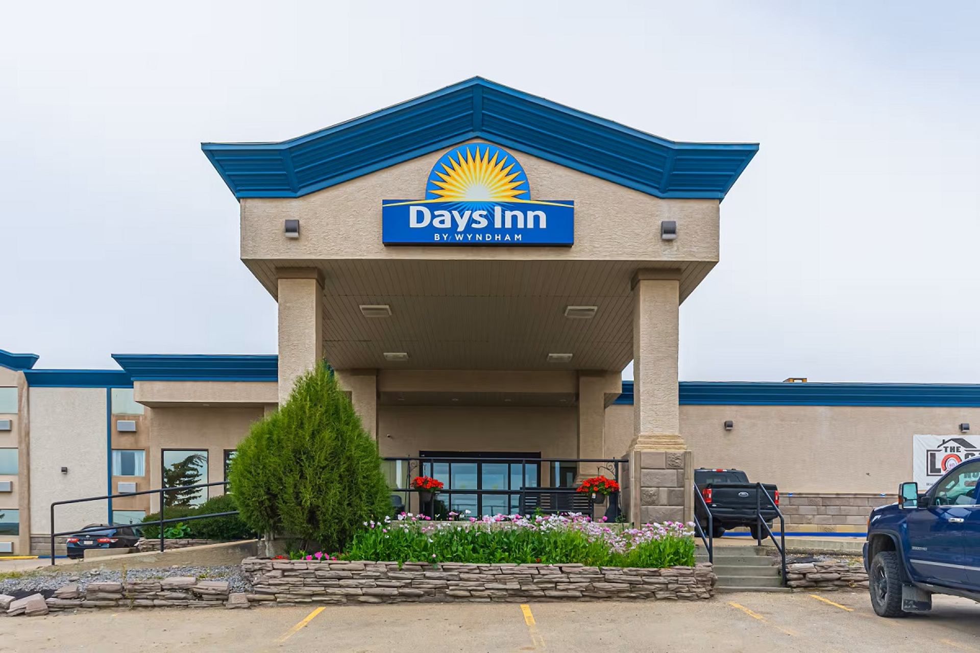 Exterior view of a Days Inn by Wyndham hotel entrance with a blue roof and landscaping.