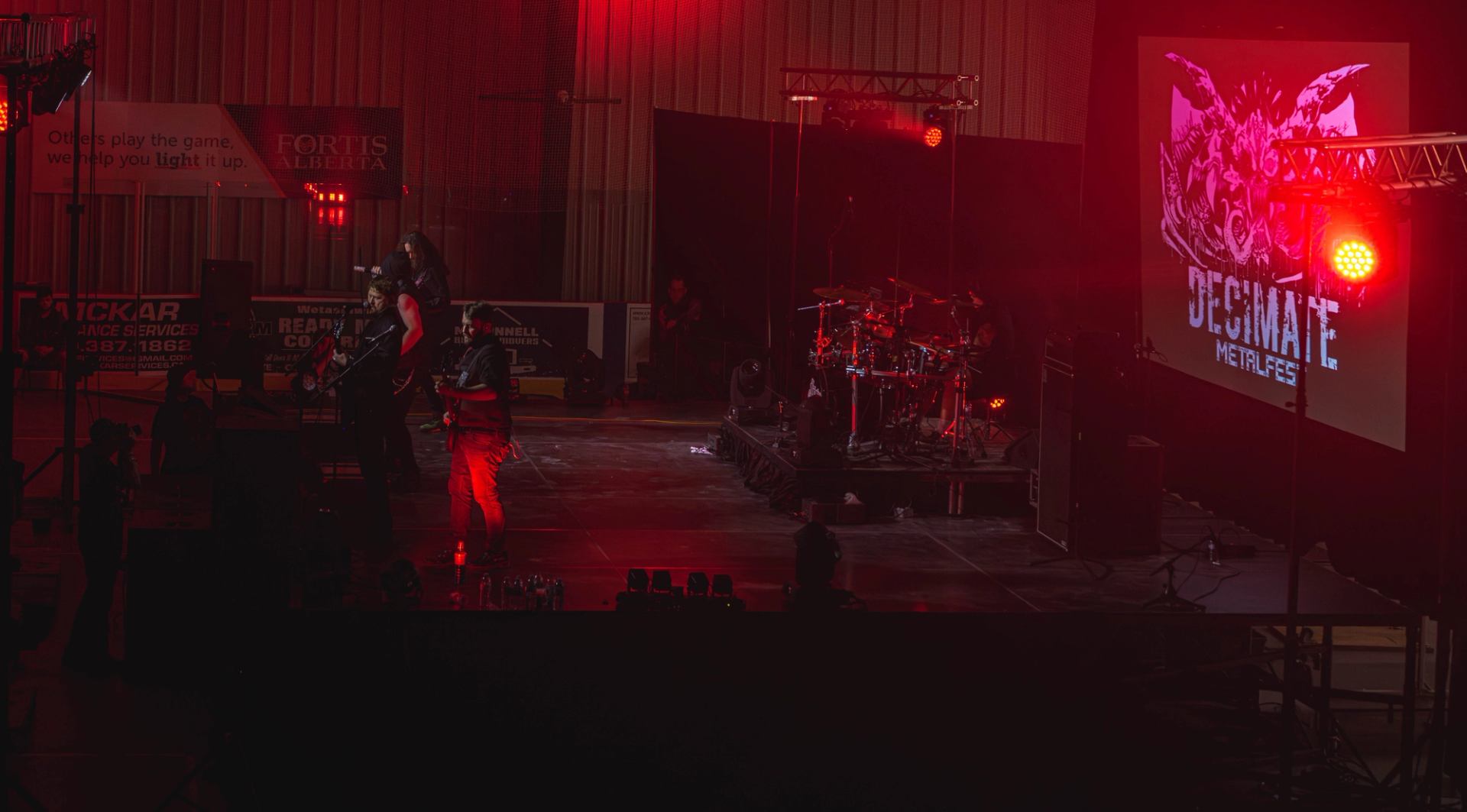 Decimate Metalfest stage glows red with band performing, drums set up, and large event logo displayed on screen.