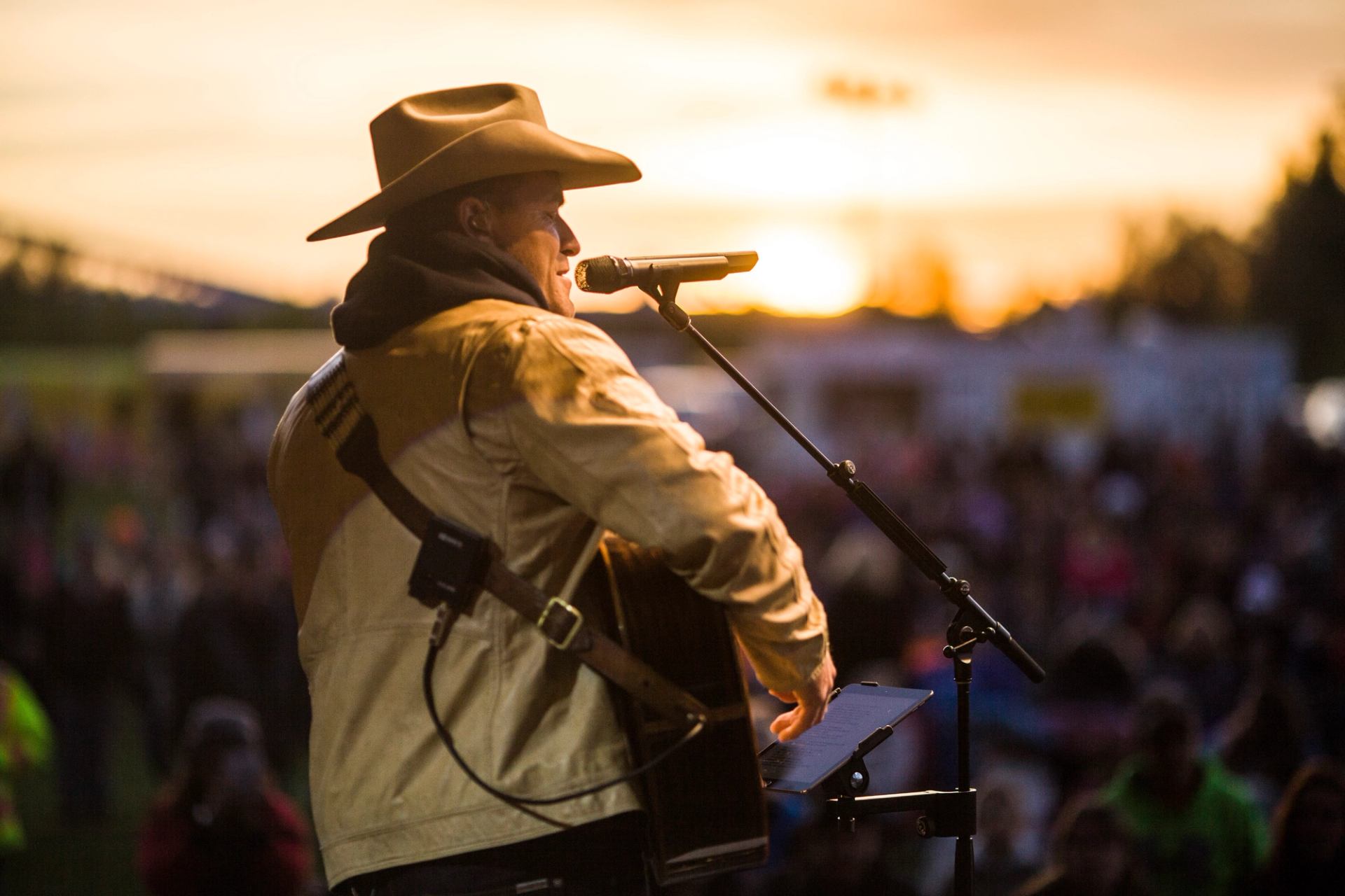 Country musician playing guitar onstage at sunset, facing the festival crowd.