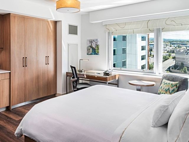 Modern hotel room with bed, desk, and city view.