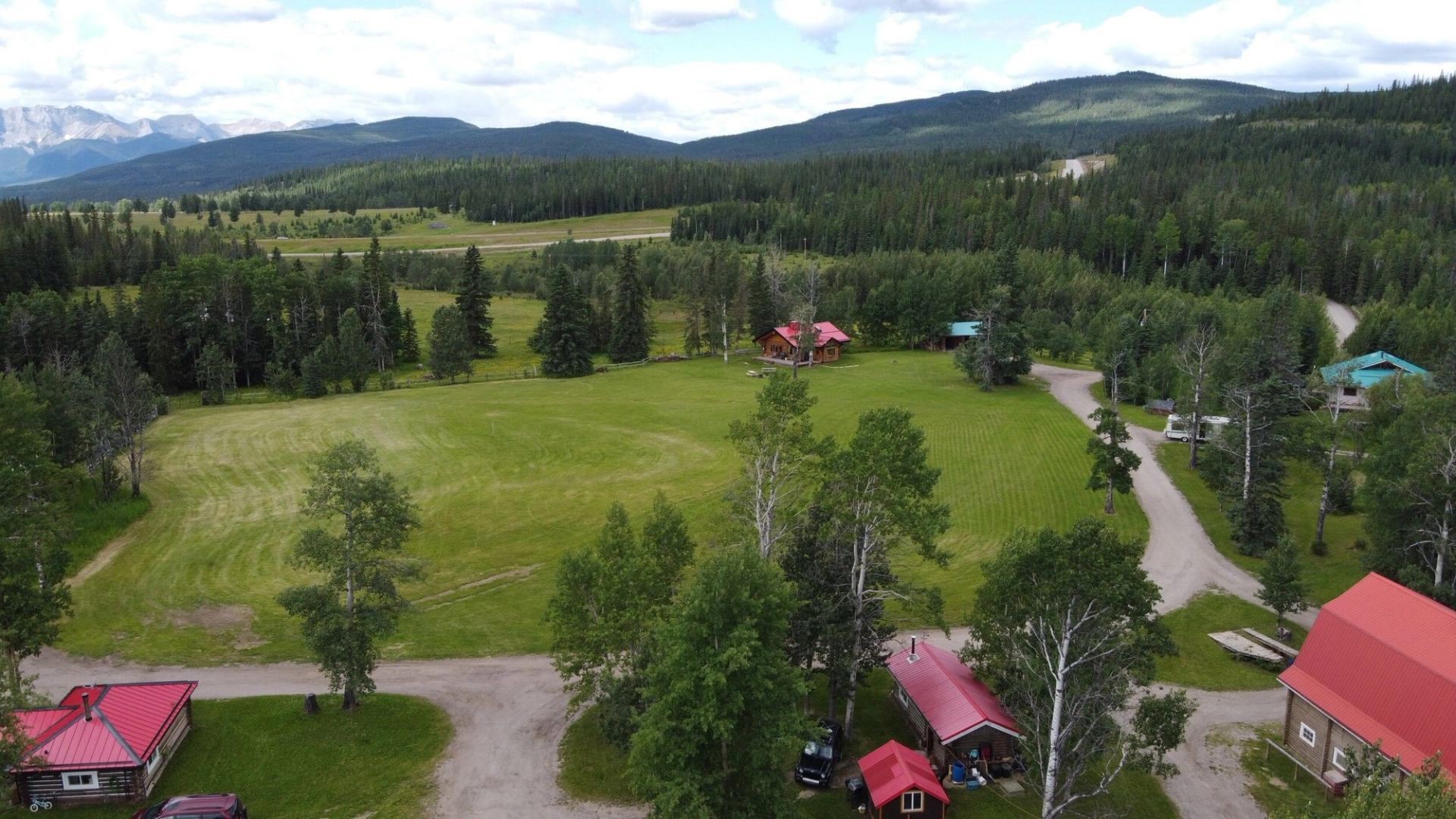Aerial view of cabins, open fields, and forested hills in the Alberta Rockies.