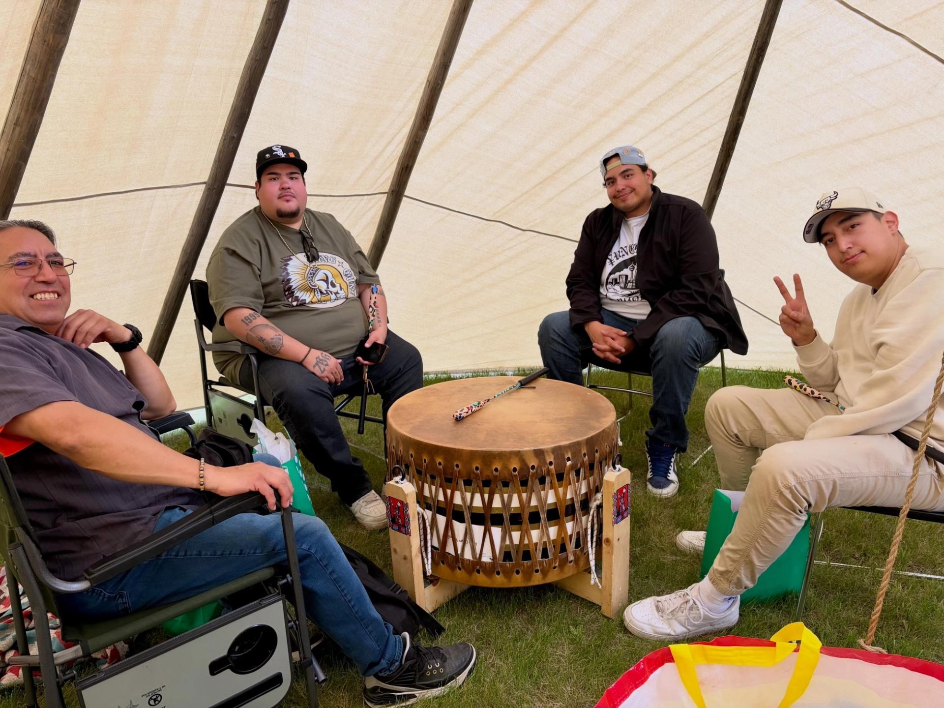 Four people sit inside a canvas tent around a large wooden hand drum.