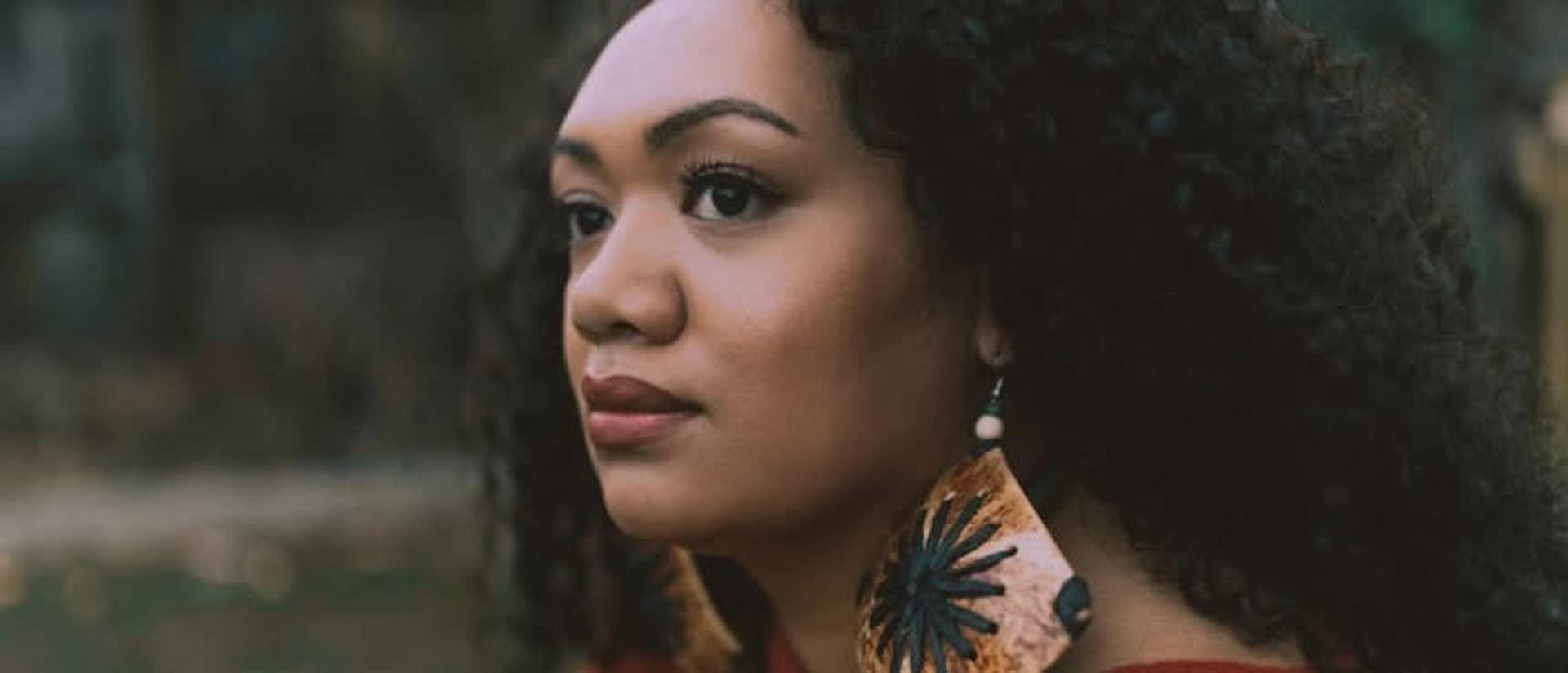 Person with curly hair wearing large patterned earrings, shown in side profile outdoors.