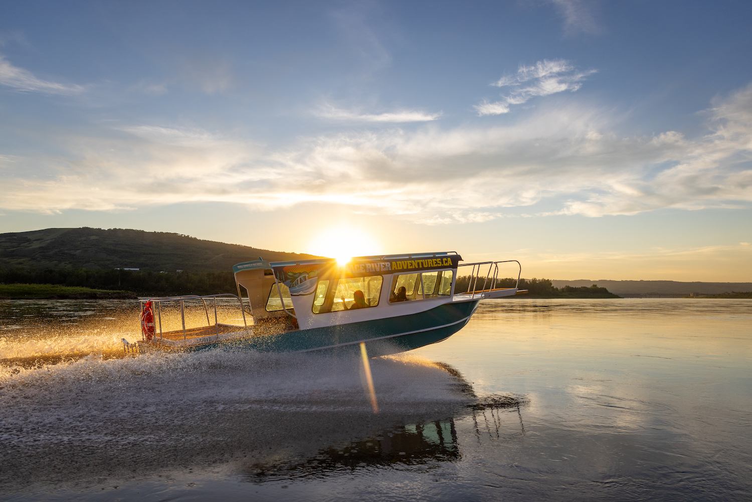Peace River Adventures boat speeding on calm river at sunset with hills in the background.