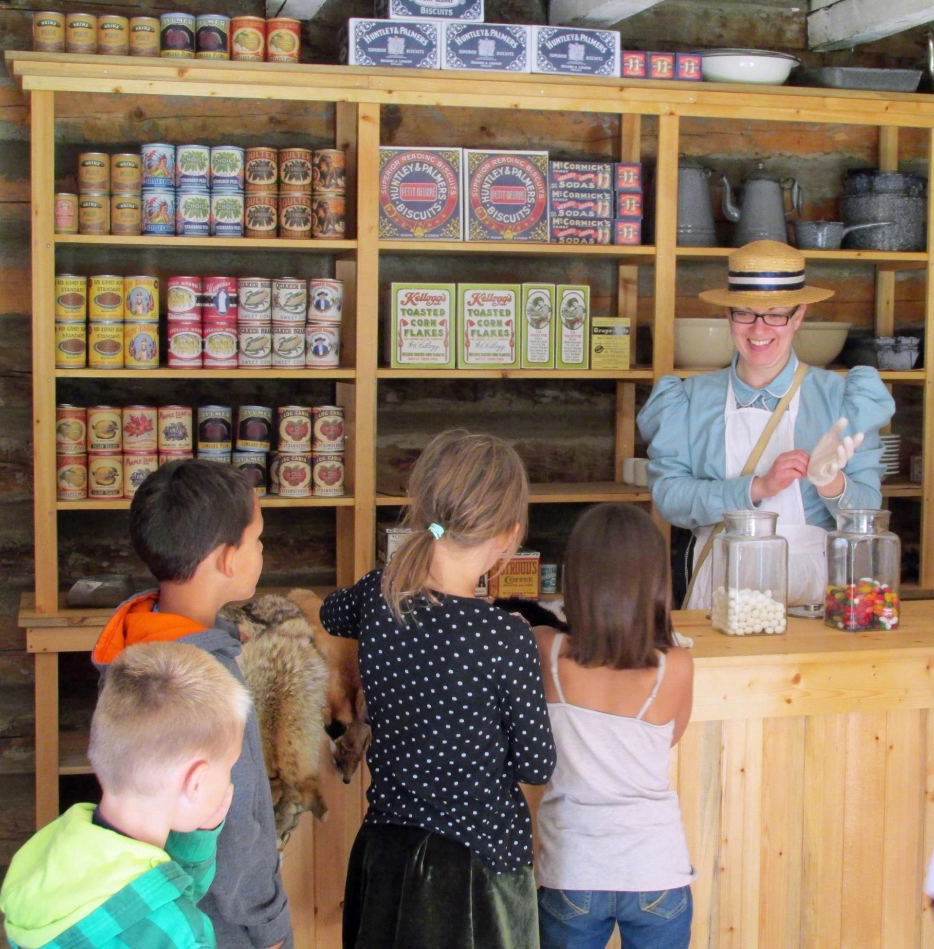 Children at a historic general store with shelves of goods at Historic Dunvegan.