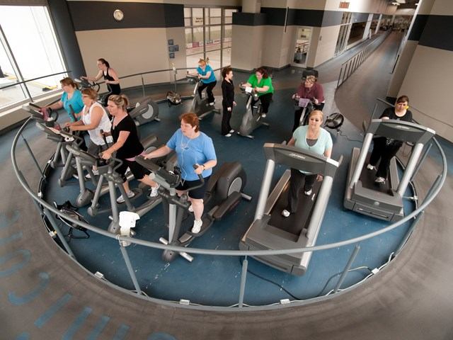 A group of people exercise on ellipticals, treadmills and stationary bikes.