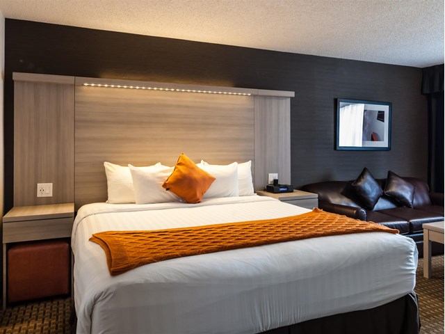 Modern hotel room with king bed, orange accents, and dark wood furnishings.