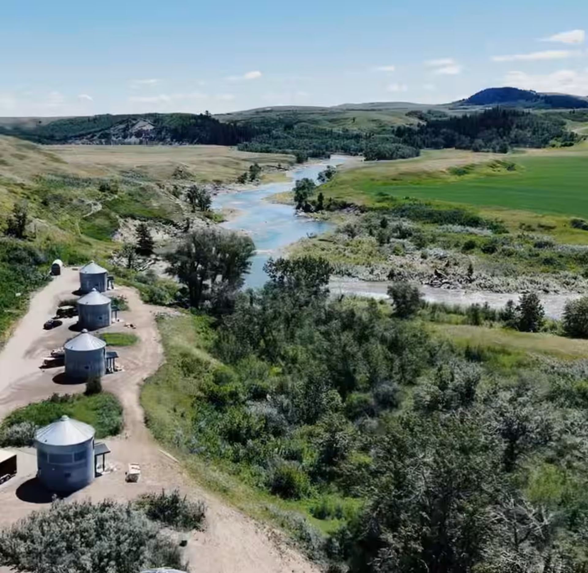 Aerial view of Saddle Hill Ranch cabins along a river with rolling hills and greenery.