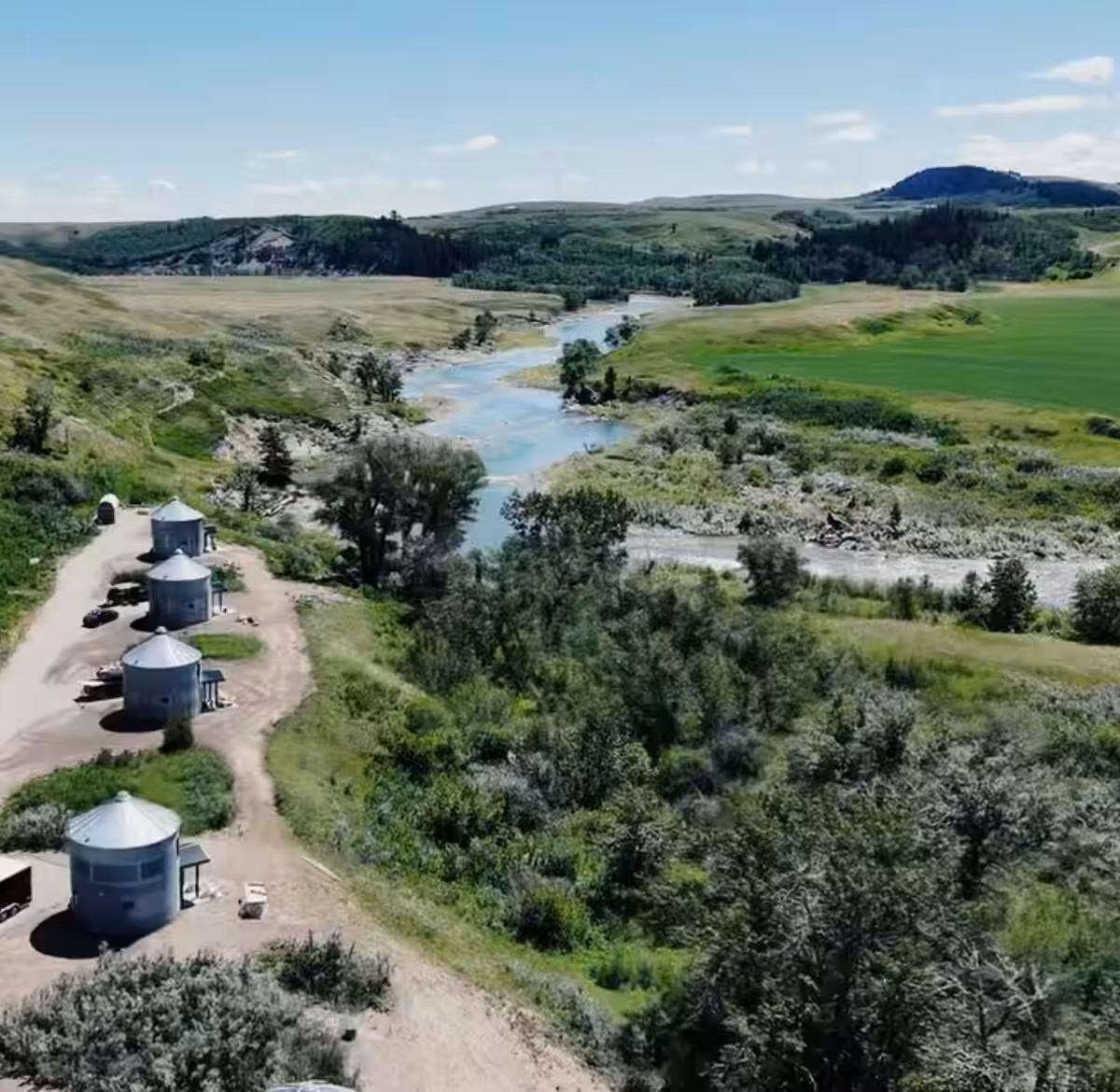 Aerial view of Saddle Hill Ranch cabins along a river with rolling hills and greenery.