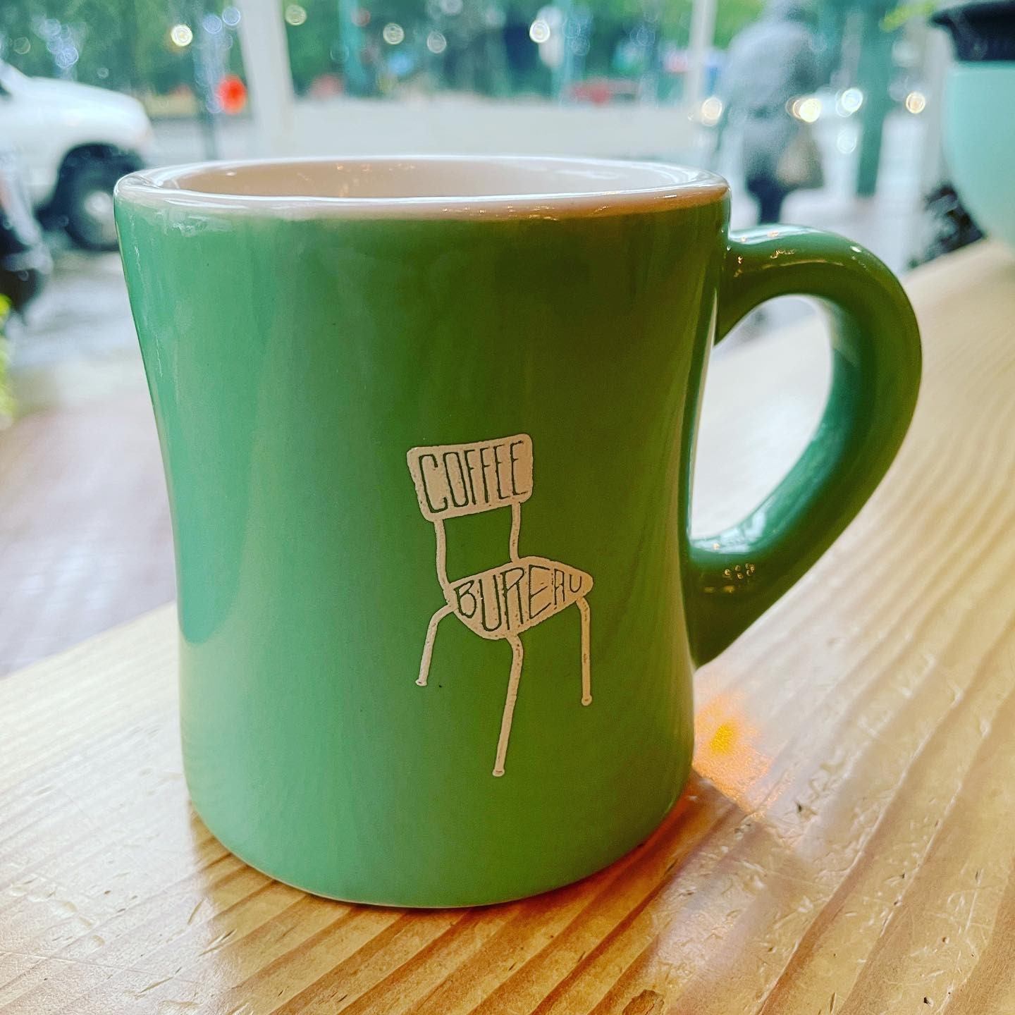 Green Coffee Bureau mug on a wooden counter inside a café.