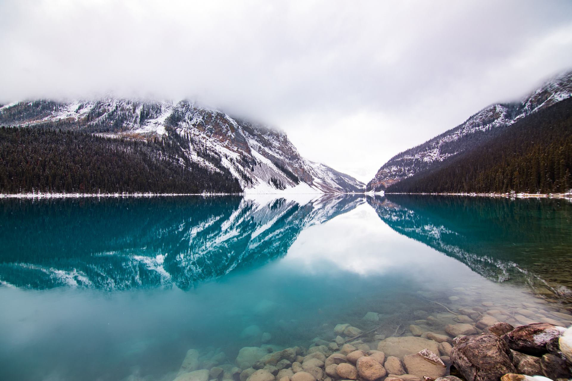 Foggy snowy peaks reflecting in Lake Louise’s turquoise water.