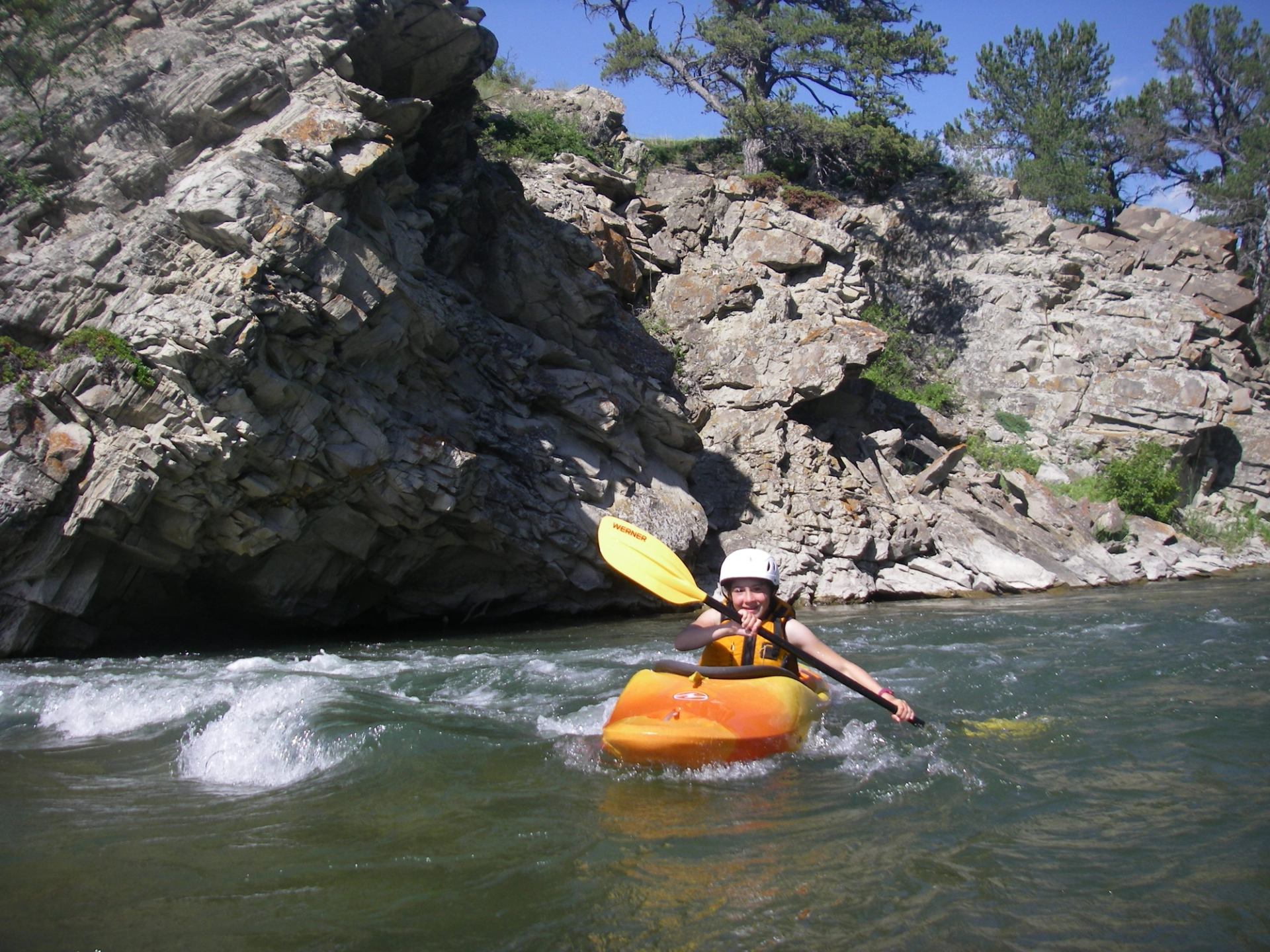 Kayaker paddling an orange kayak beside rocky canyon cliffs.