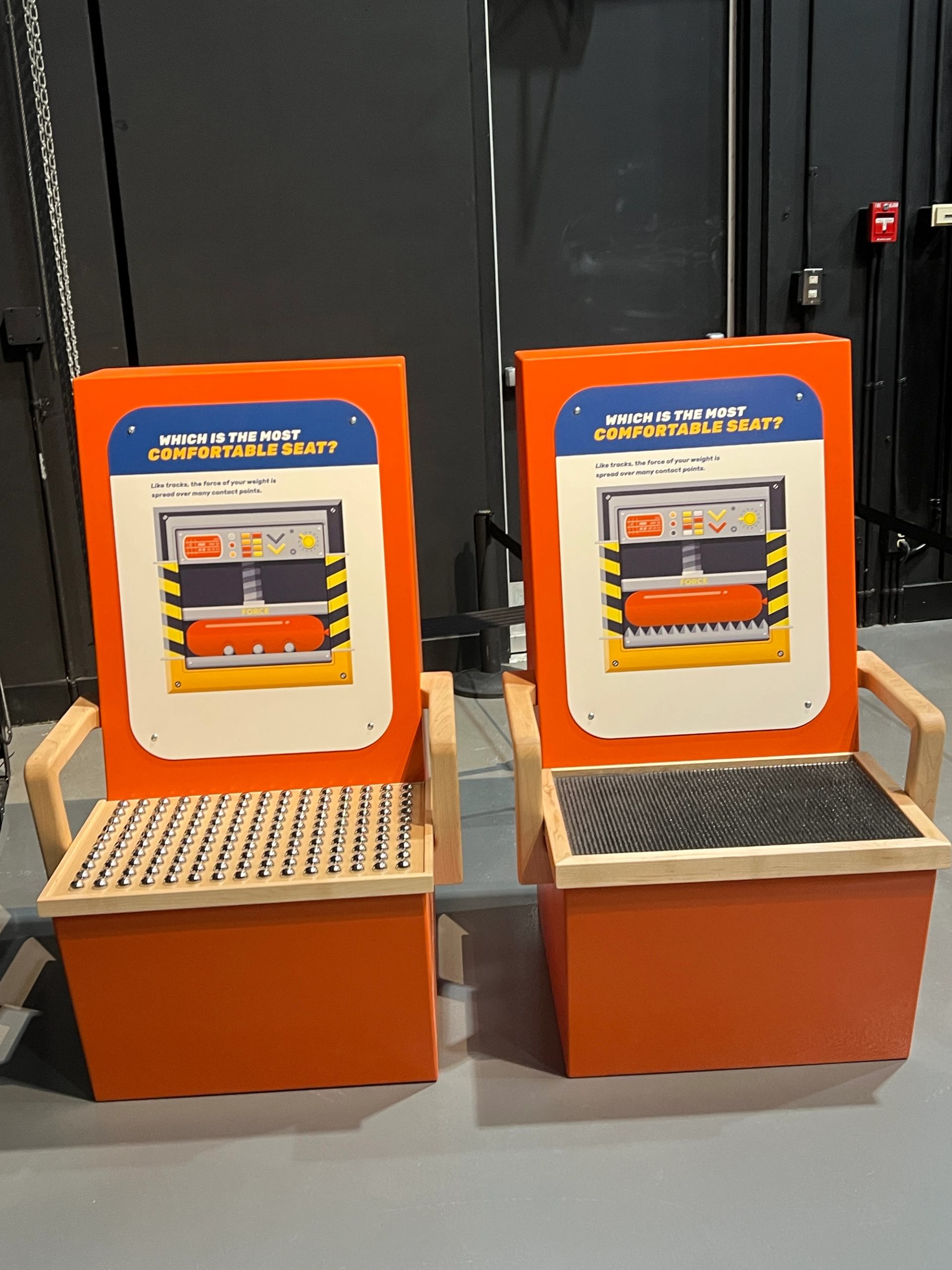 Orange interactive exhibits with graphic panels reading "Which is the most comfortable seat?"