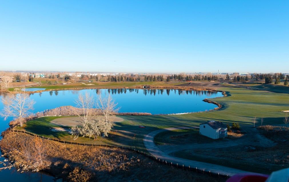 Aerial view of a golf course with a large blue lake, winding cart path, and open fairways.