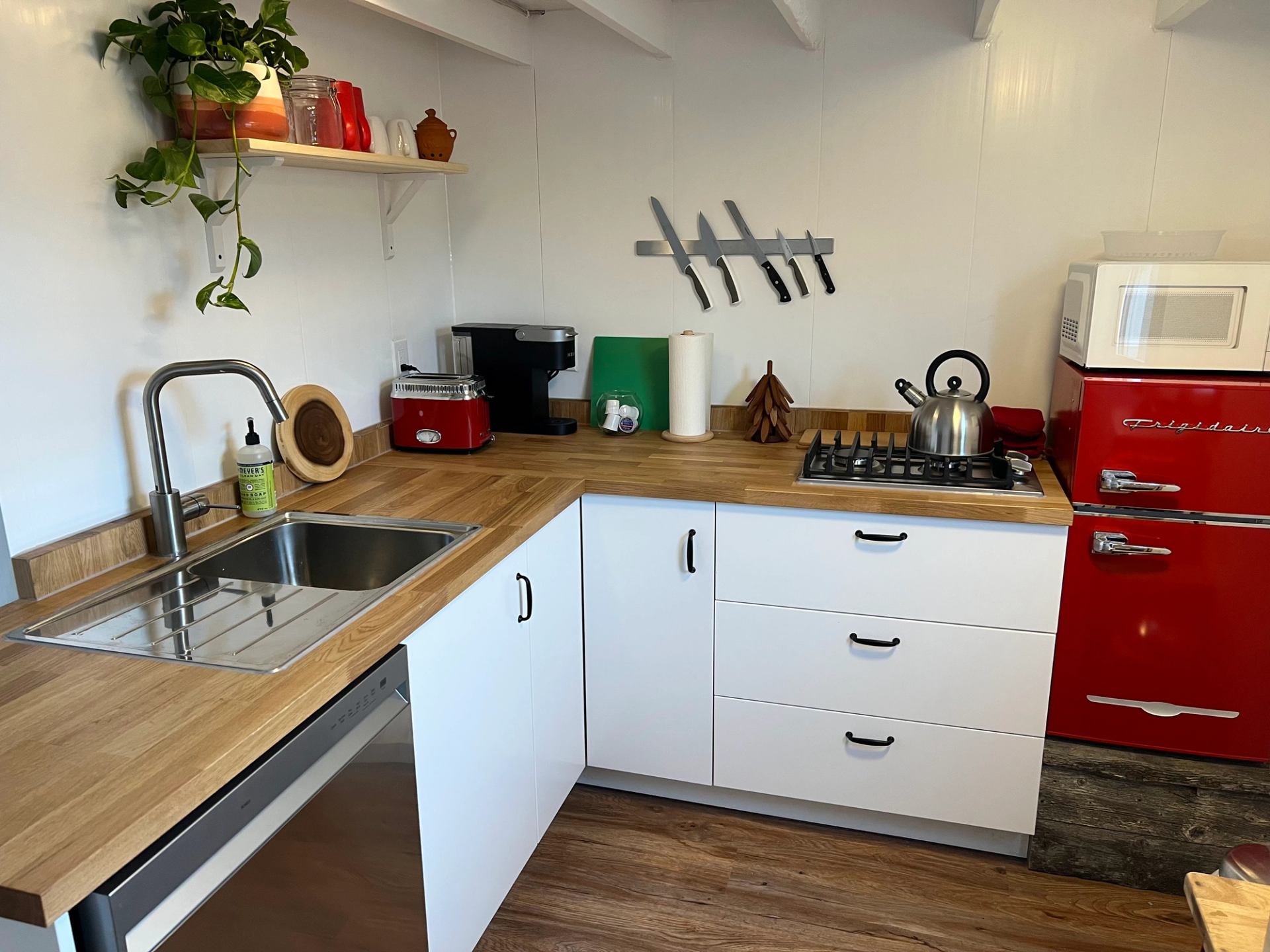 Cabin kitchen with wood countertops, white cabinets, red appliances, and a mounted knife rack.