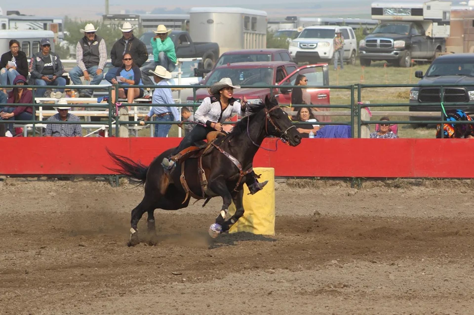 Rodeo rider on galloping horse rounding yellow barrel as spectators watch from stands.