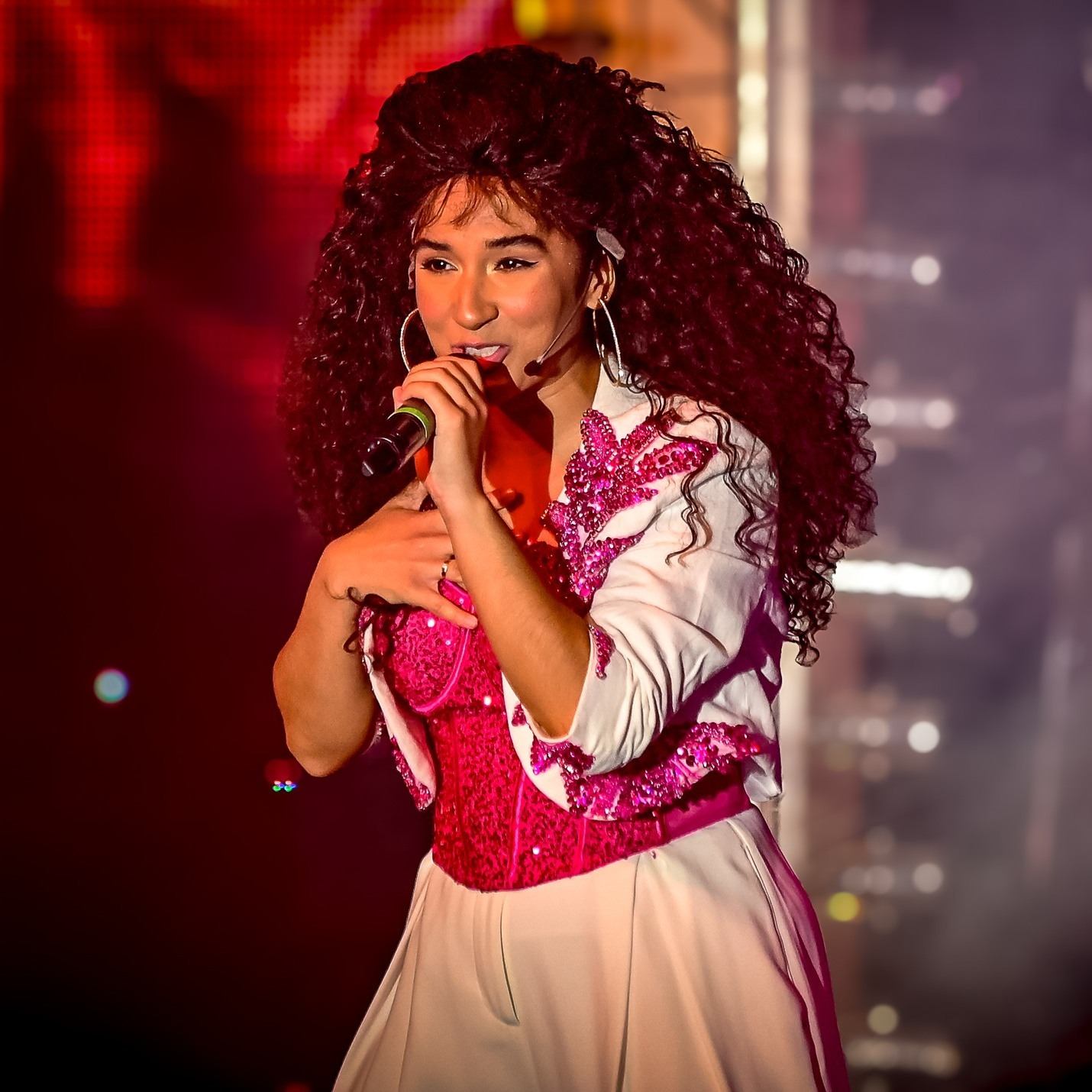 Curly-haired performer holding mic in concert lighting.
