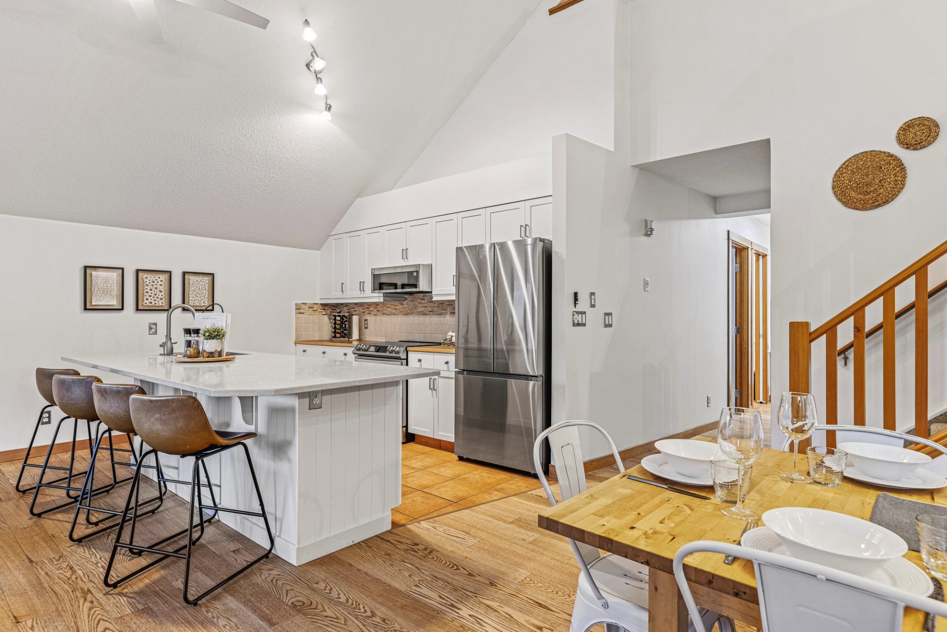 Modern white kitchen with island, stainless appliances and adjacent wooden dining table.