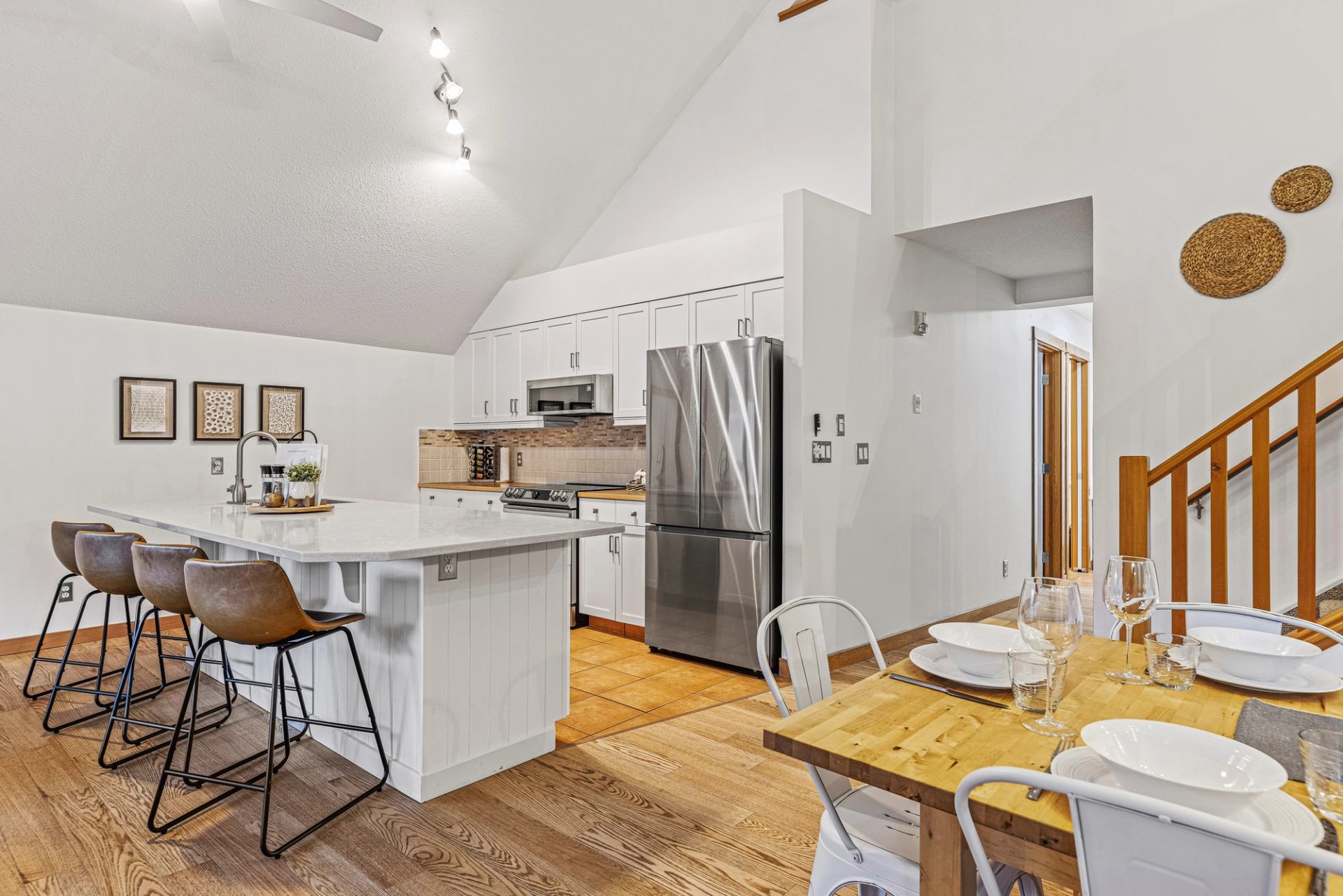 Modern white kitchen with island, stainless appliances and adjacent wooden dining table.
