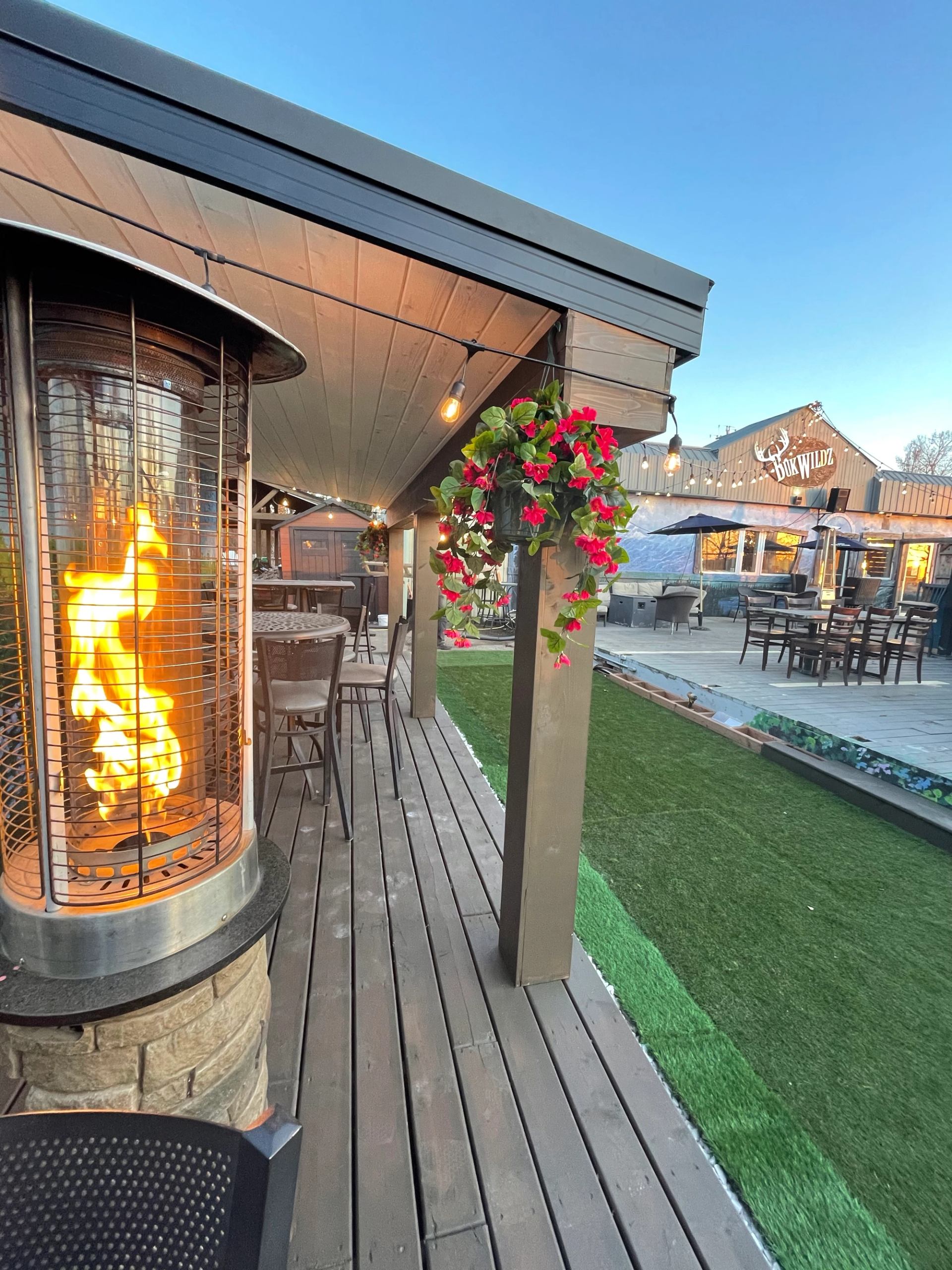 Outdoor patio with heater, hanging flowers, and dining tables at Bukwildz.