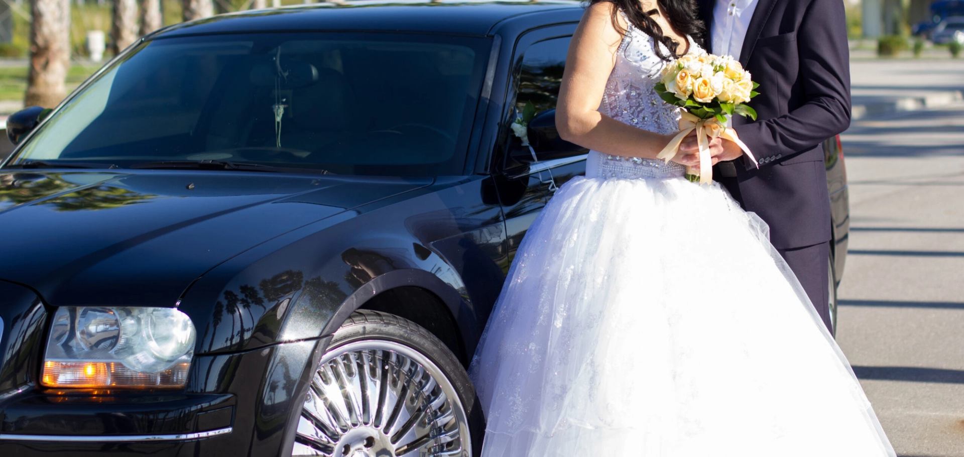 Bride and groom beside black luxury car, perfect for wedding day travel.