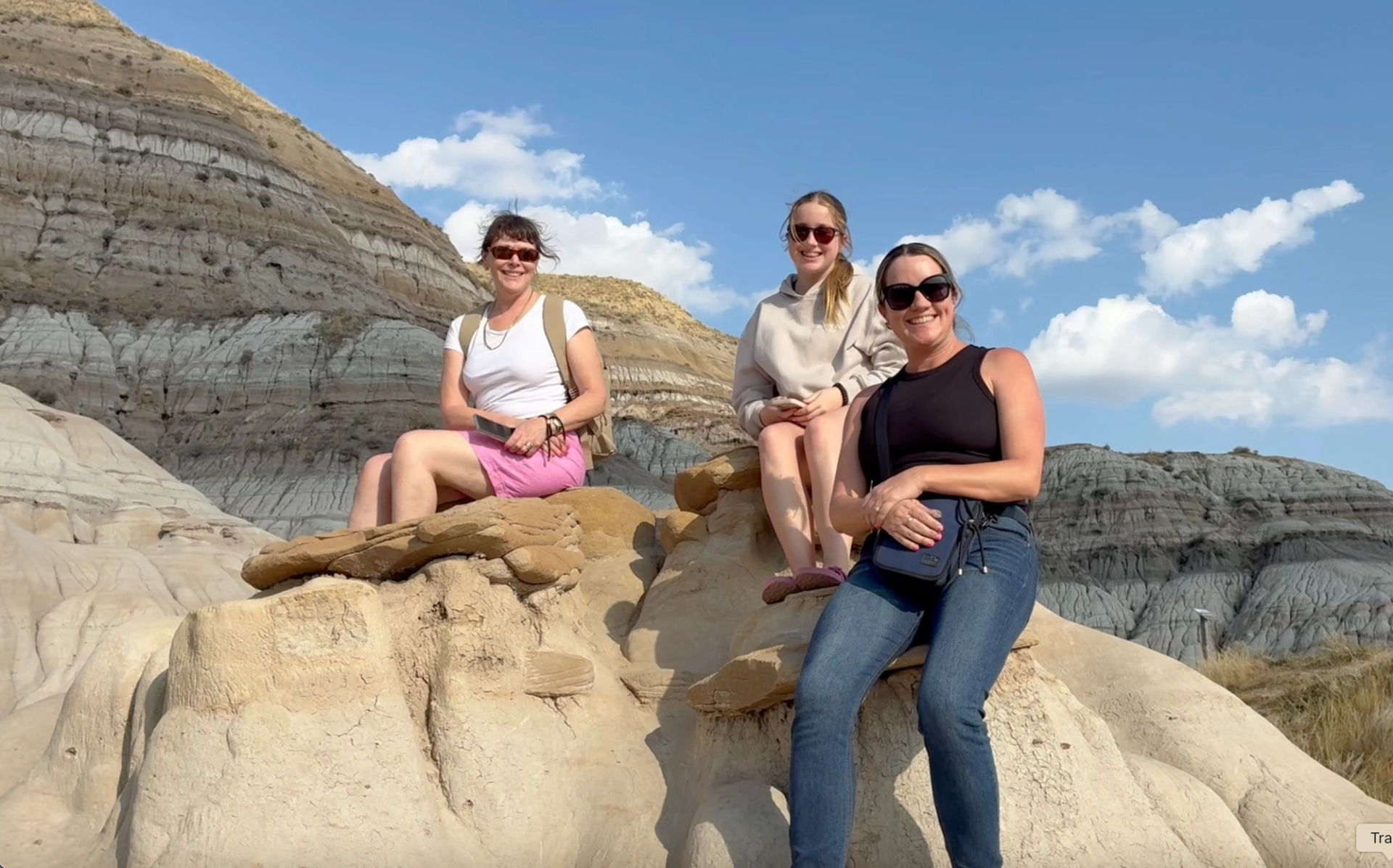 Three people sit on layered sandstone rocks in a dry, rocky canyon landscape.