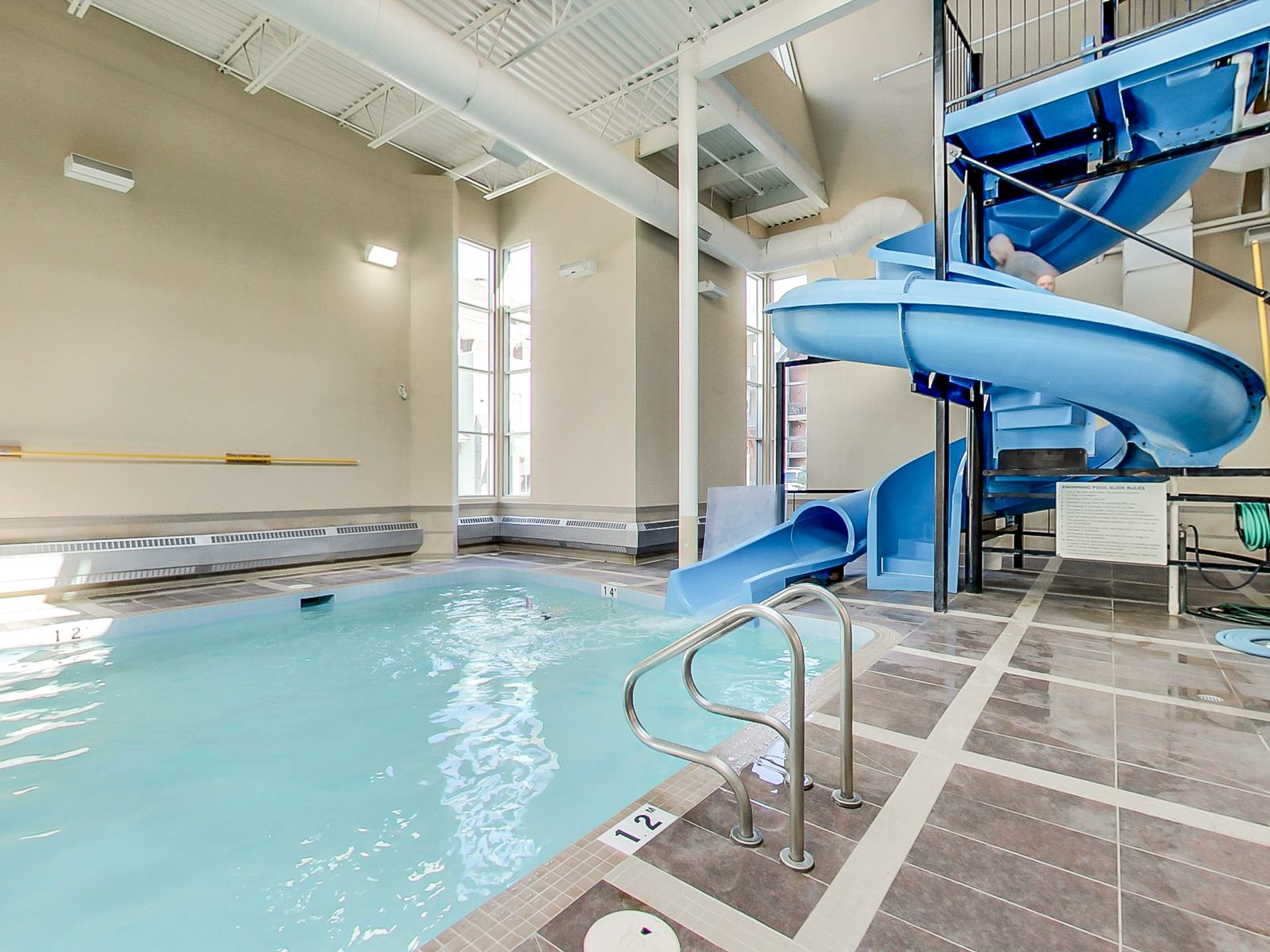 Indoor swimming pool with blue waterslide, tiled deck and metal handrails.