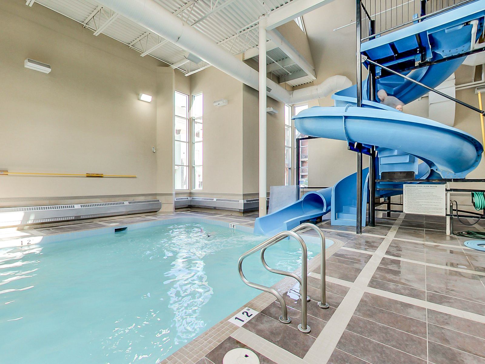 Indoor swimming pool with blue waterslide, tiled deck and metal handrails.