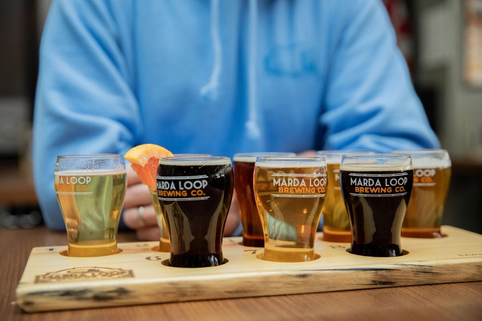 Marda Loop Brewing Co. beer flight sits before a person in a blue hoodie.