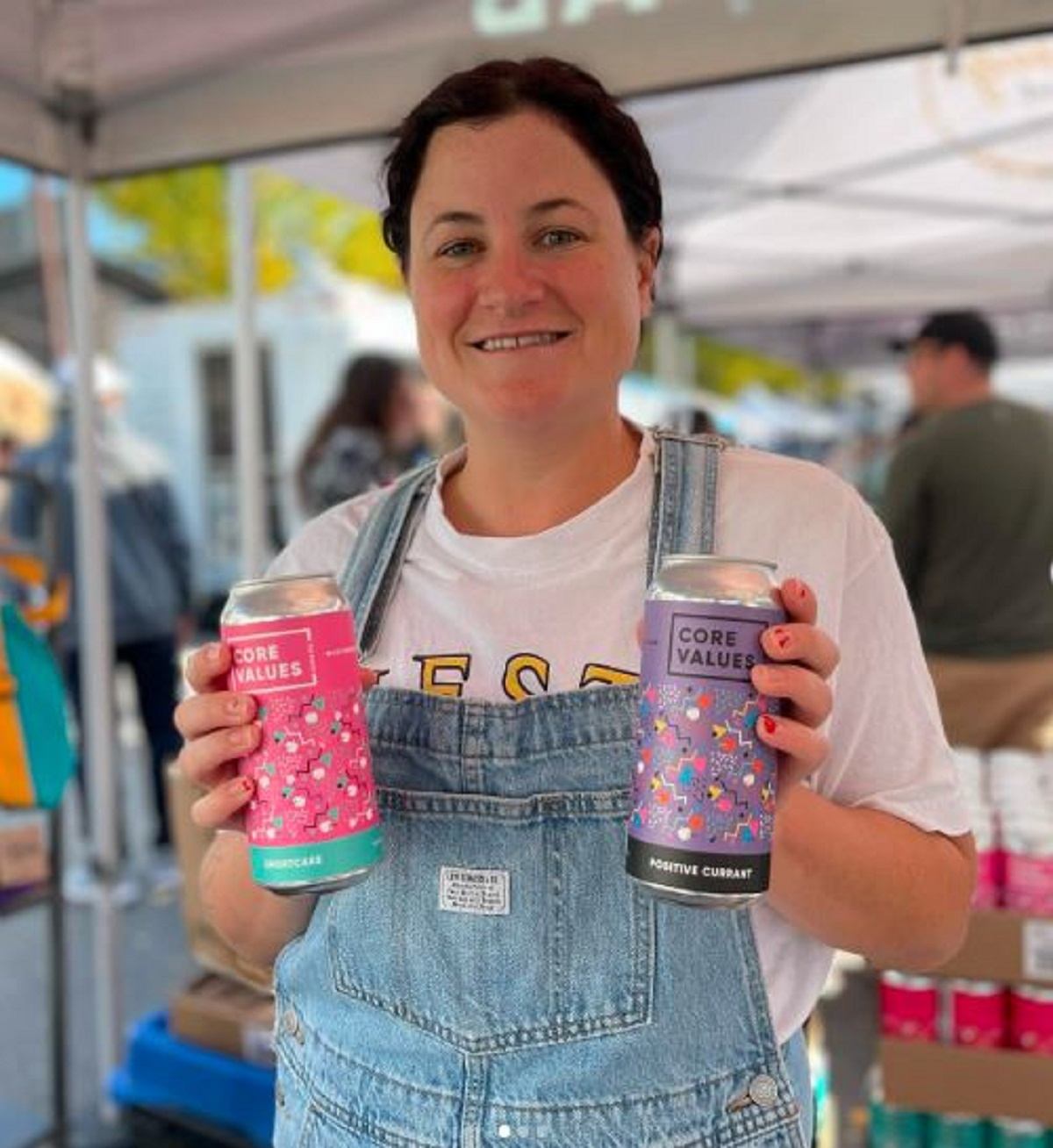 A lady holding two cans of cider at the market.