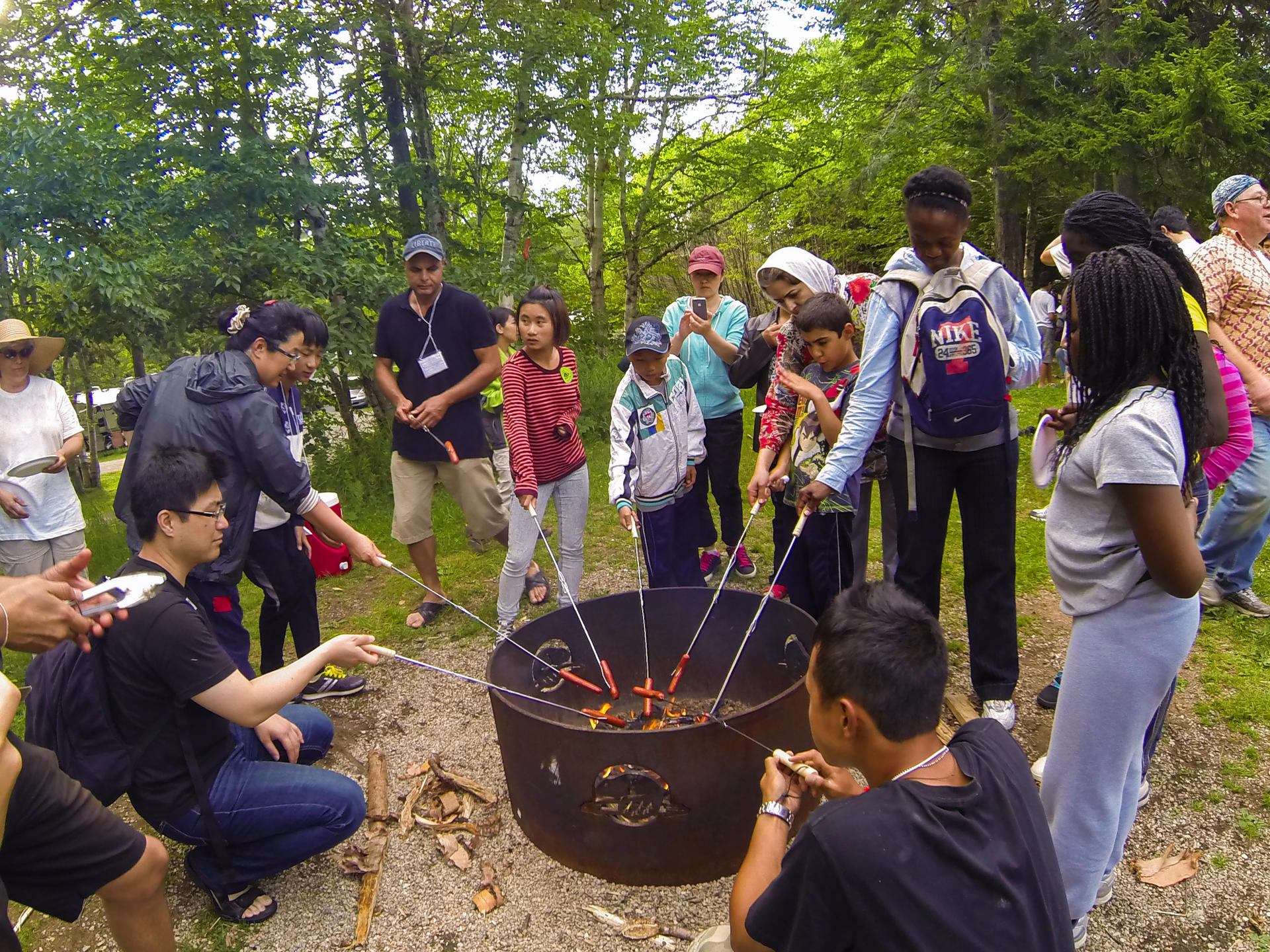 A group of people having a wienner roast around the firepit