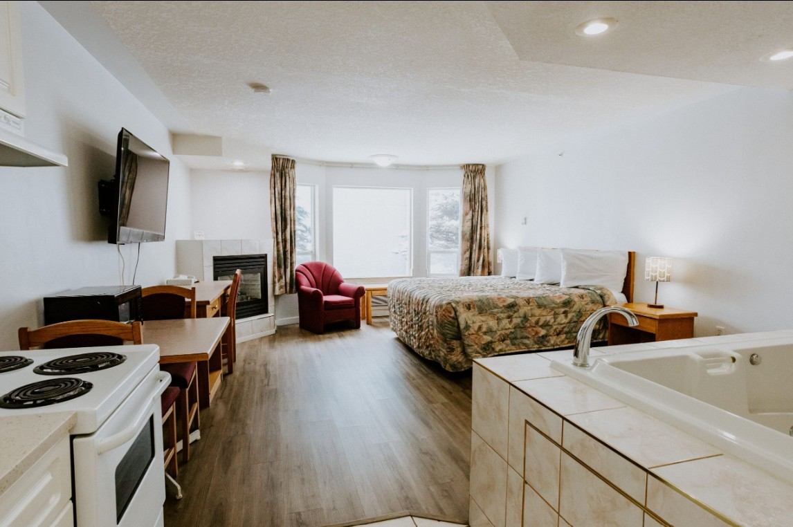 Studio-style hotel room with bed, kitchenette, fireplace, red armchair and corner whirlpool tub.