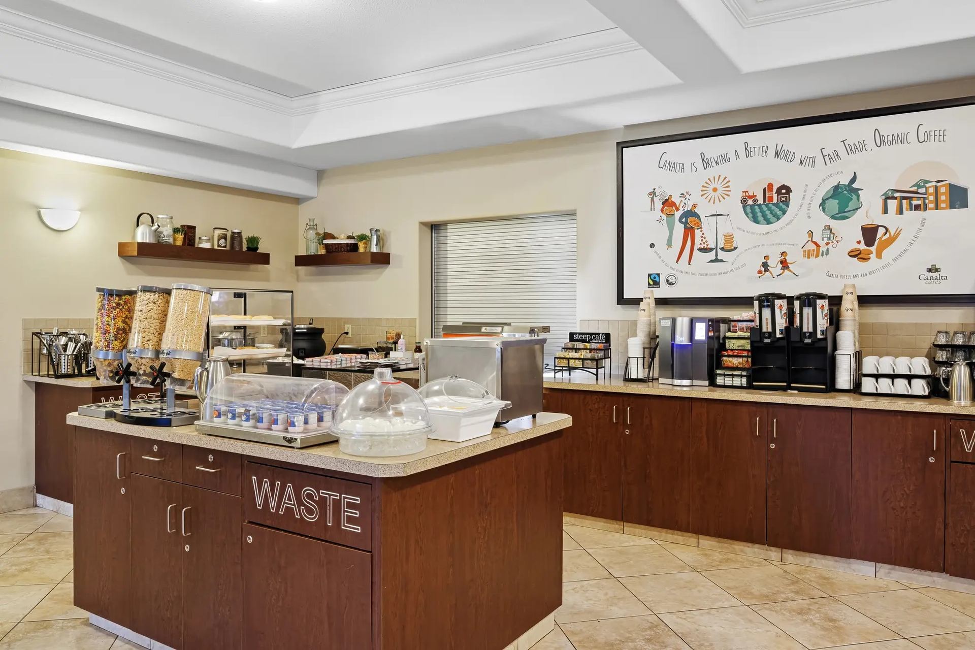 Hotel breakfast buffet area with cereal dispensers, covered pastries and coffee station.