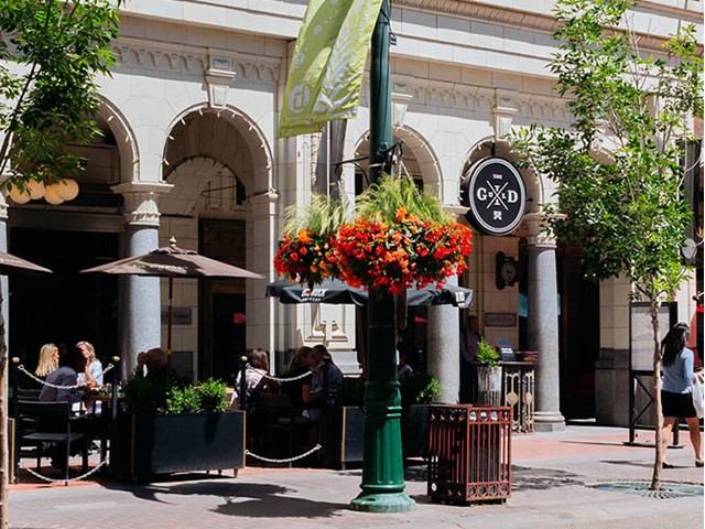 Outdoor café with umbrellas, flowers, and people dining on a city street.