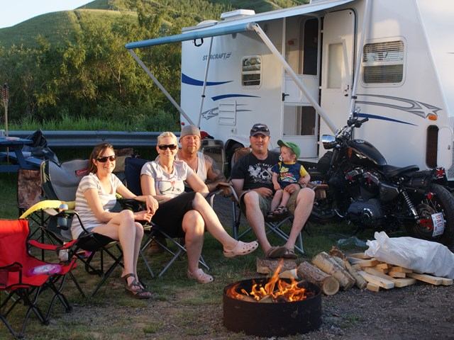 A family sitting around a campfire with their RV behind them.