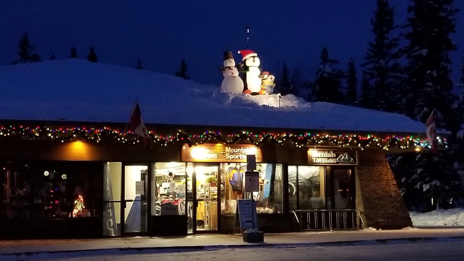 Snow-covered shop with festive lights, snowmen, and Santa decorations at night.