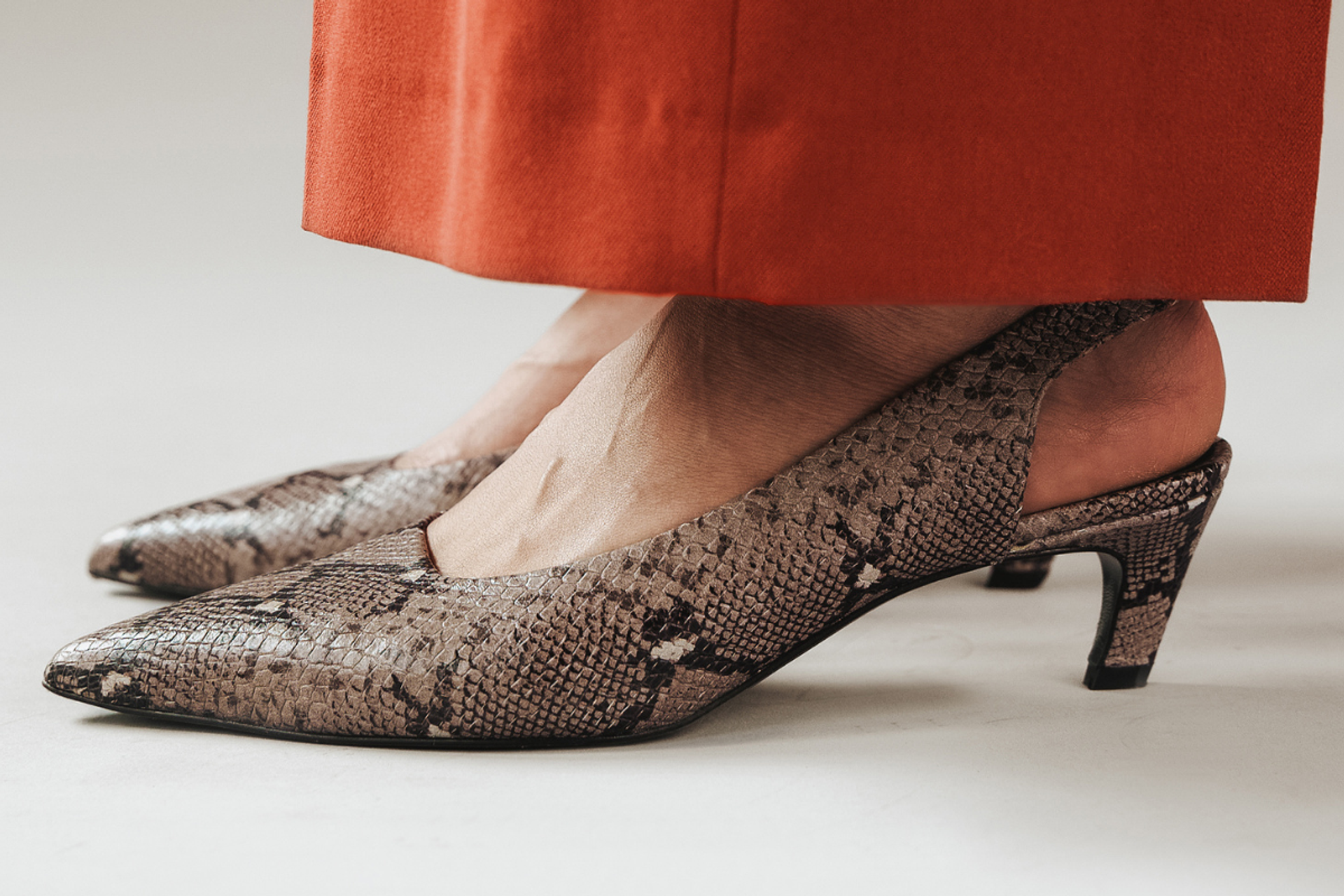 Snakeskin pointed-toe shoes with open back, worn with cropped orange pants.