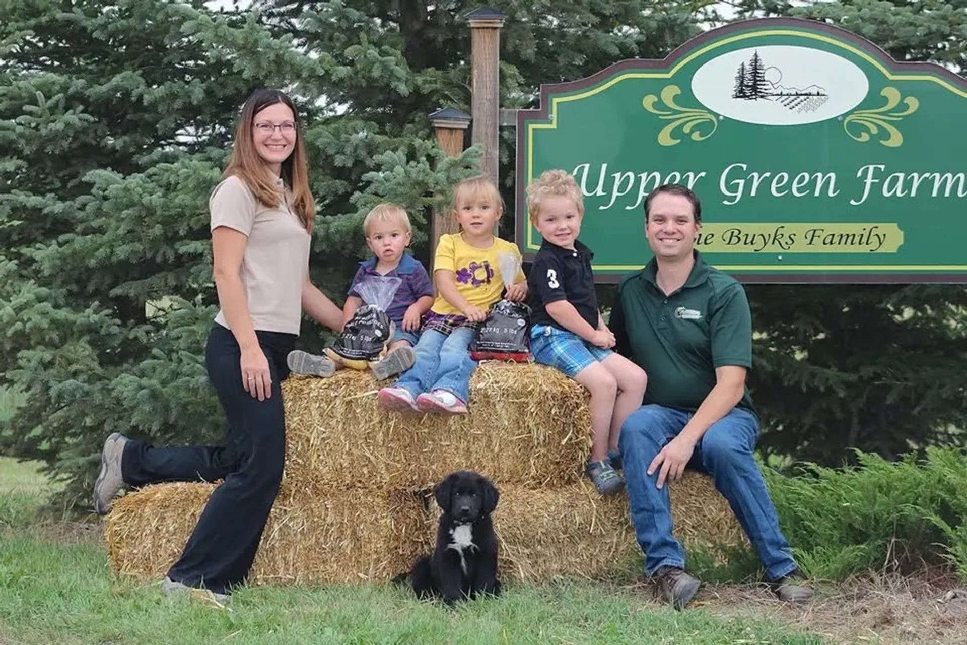 Group of people and dog on hay bales in front of Upper Green Farms sign.