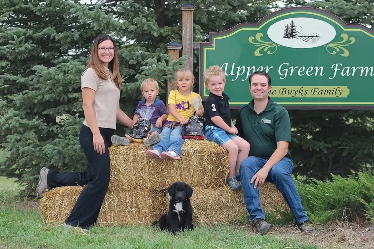 Group of people and dog on hay bales in front of Upper Green Farms sign.