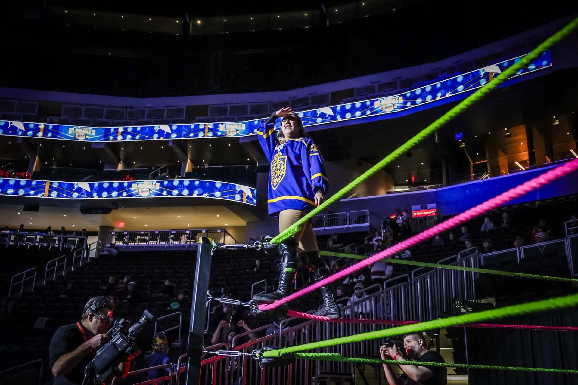 Wrestler stands on the corner ropes posing under arena lights.