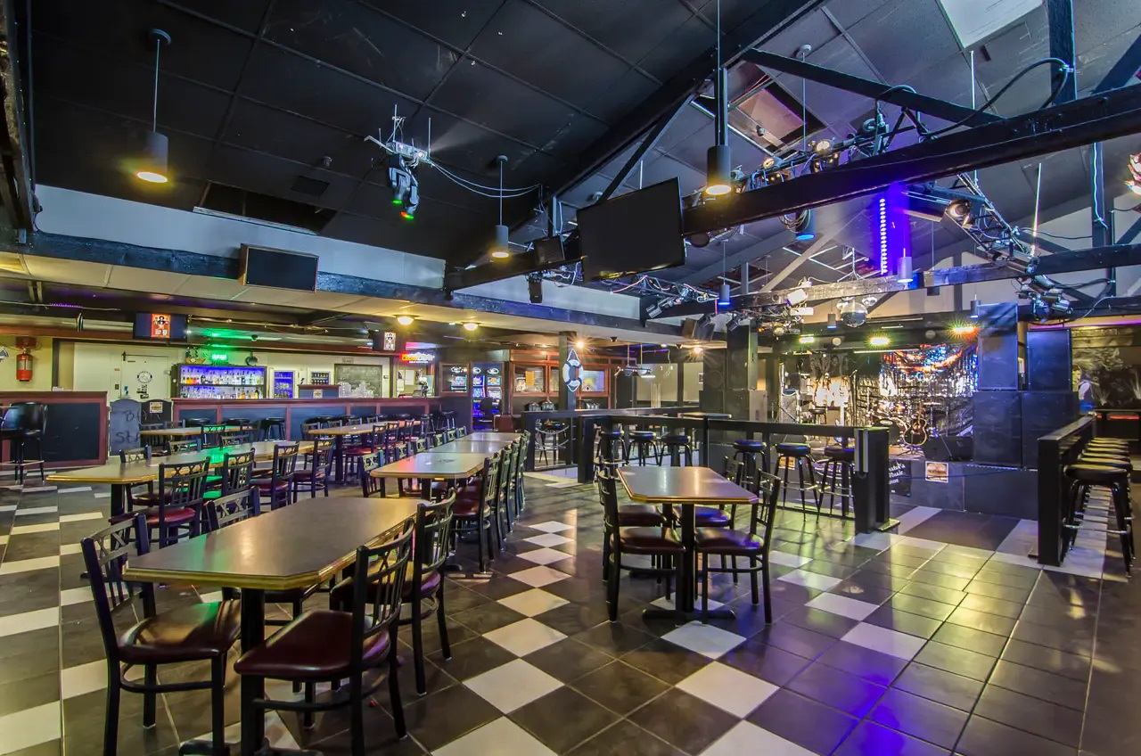Large lounge with dining tables, checkerboard flooring, stage lighting, and entertainment space.